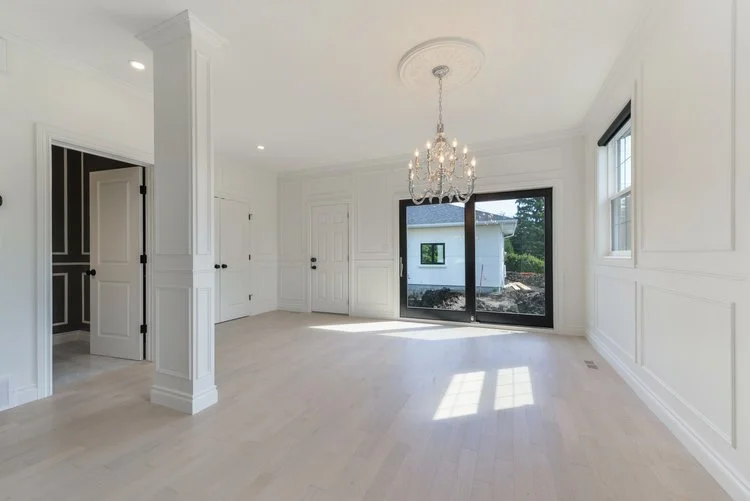 Empty dining room with white walls, wood flooring, a chandelier, large glass sliding door, and two windows letting in natural light.