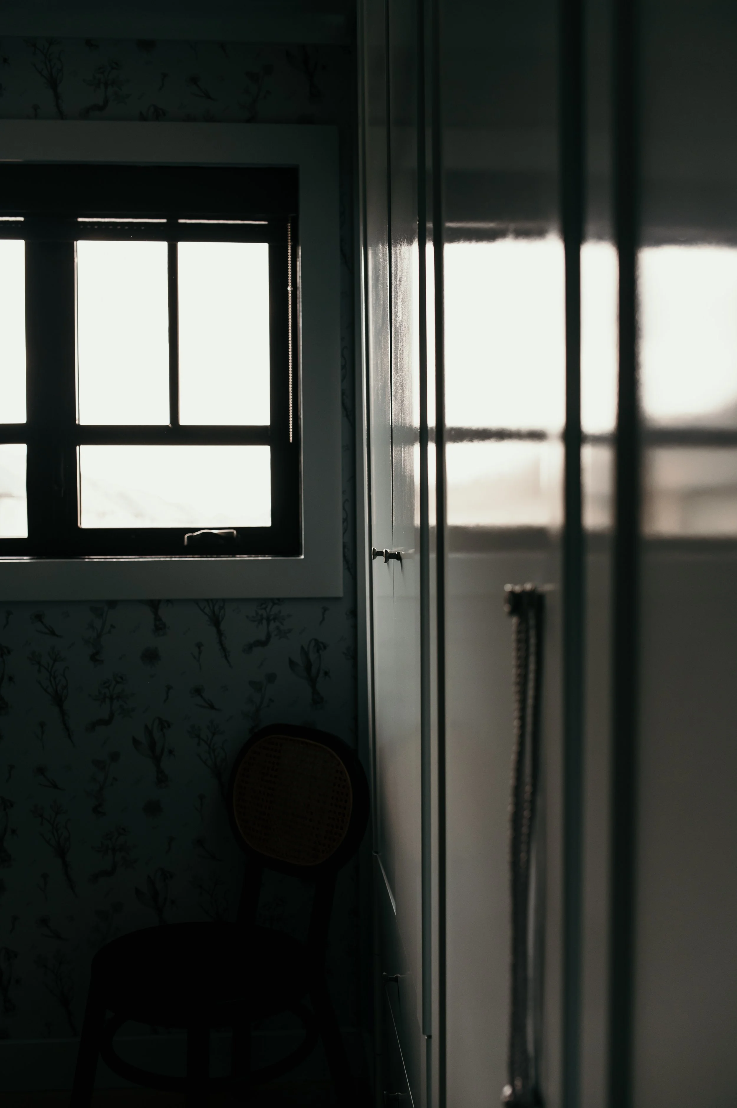 A silhouette of a chair against a window with closed blinds inside a dimly lit room.