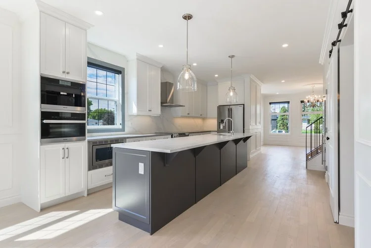 Modern kitchen with white cabinets, black island, stainless steel appliances, and large windows allowing natural light.