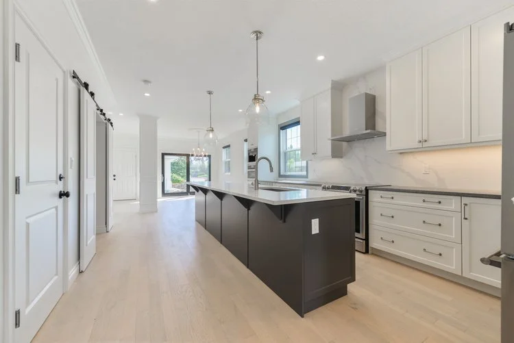 Modern kitchen with white cabinets, marble backsplash, black island with sink, and hanging pendant lights.
