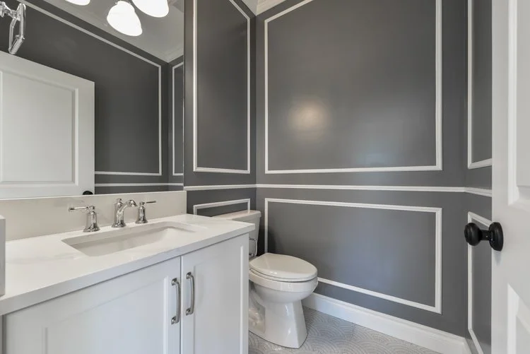 A modern bathroom with dark gray walls featuring white trim patterns, a white vanity with a sink, and a toilet.