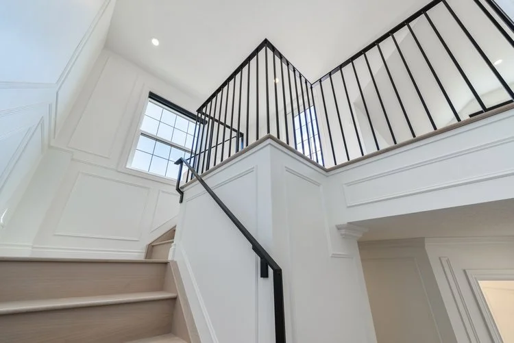 Interior view of a staircase with white walls, a black railing, and a large window bringing in natural light.
