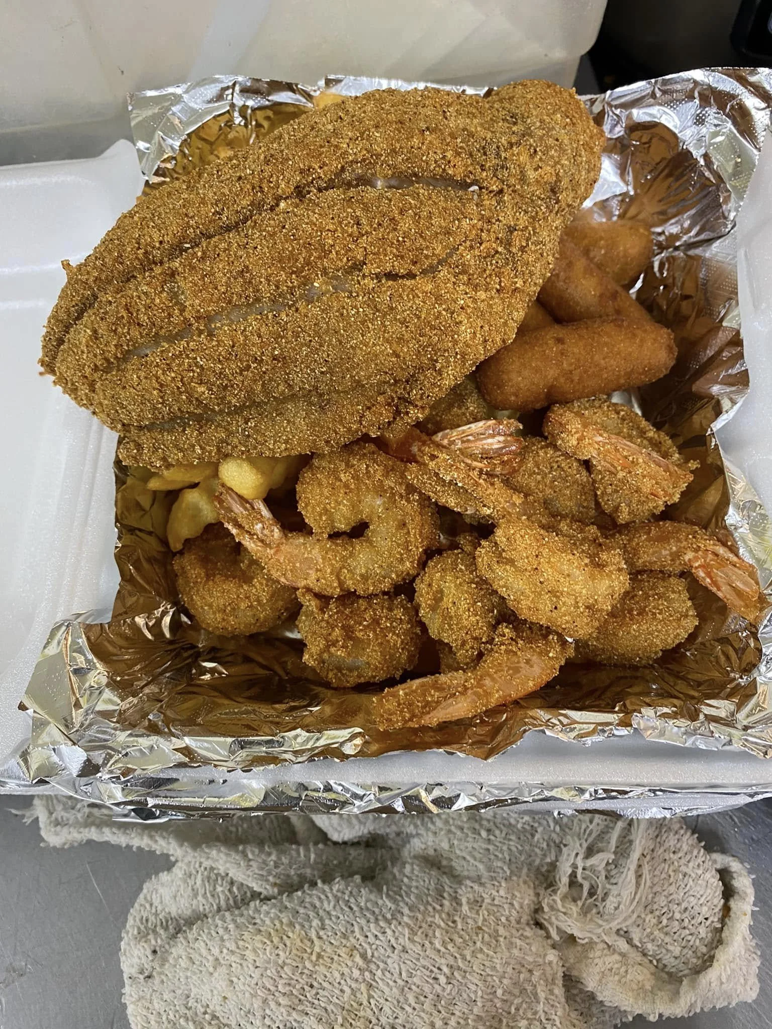 Fried breaded fish fillet, fried shrimp, and fried chicken pieces served on aluminum foil.