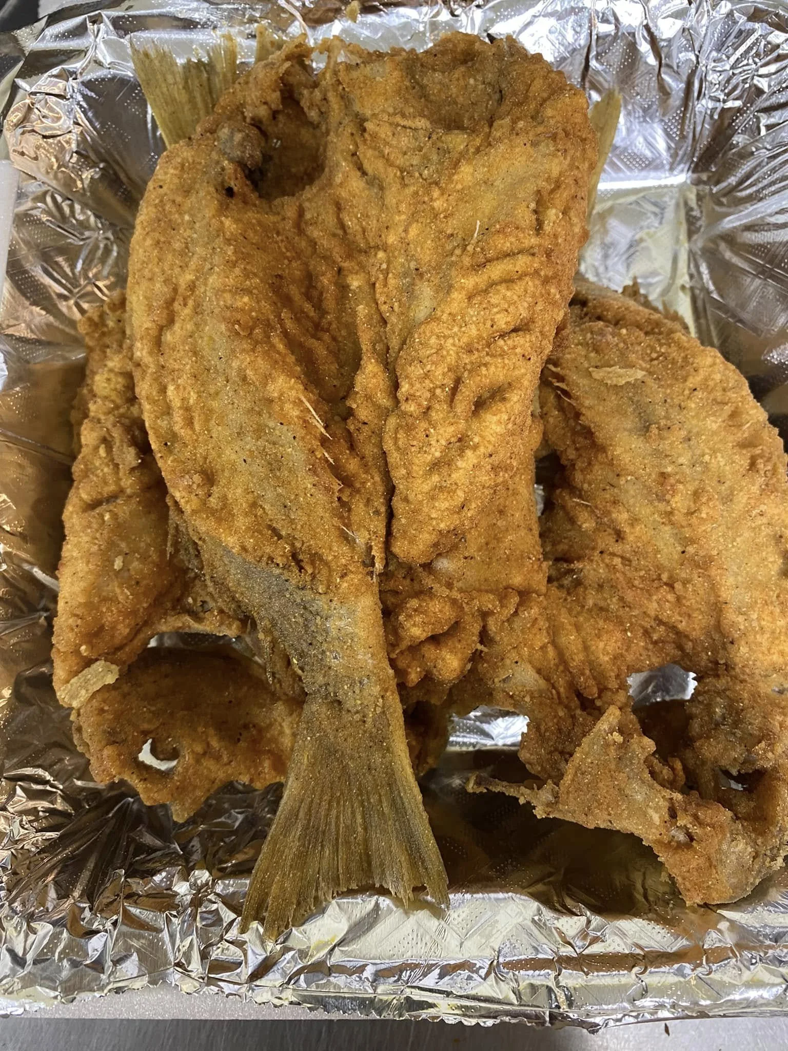 Fried fish fillets on aluminum foil with a fish head visible in the foreground.