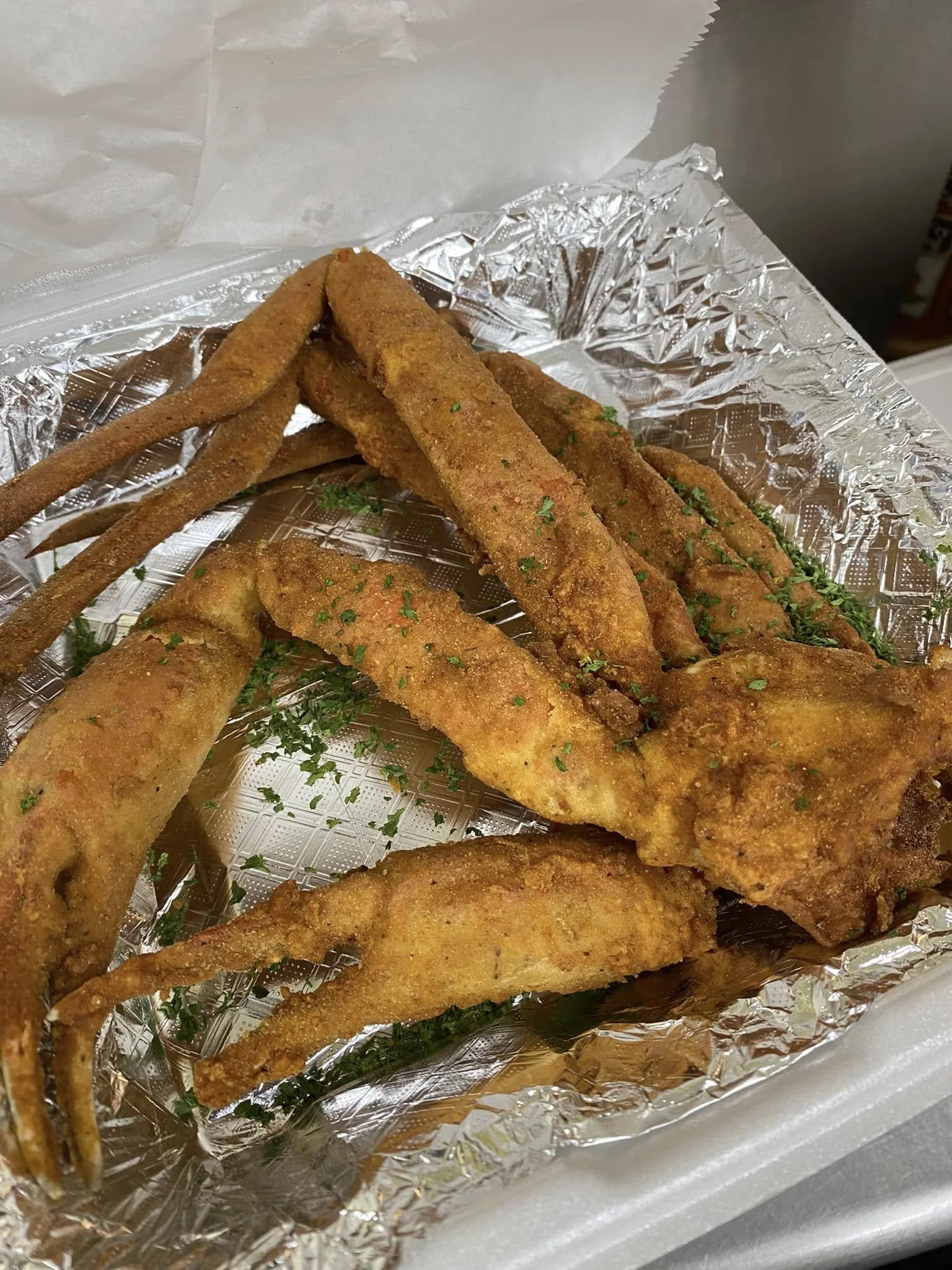 Fried fish fillets with seasoned breading garnished with chopped parsley, placed on aluminum foil.