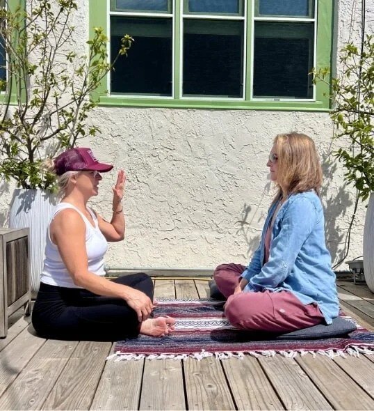 Two women seated facing each other on a deck during a breath practice