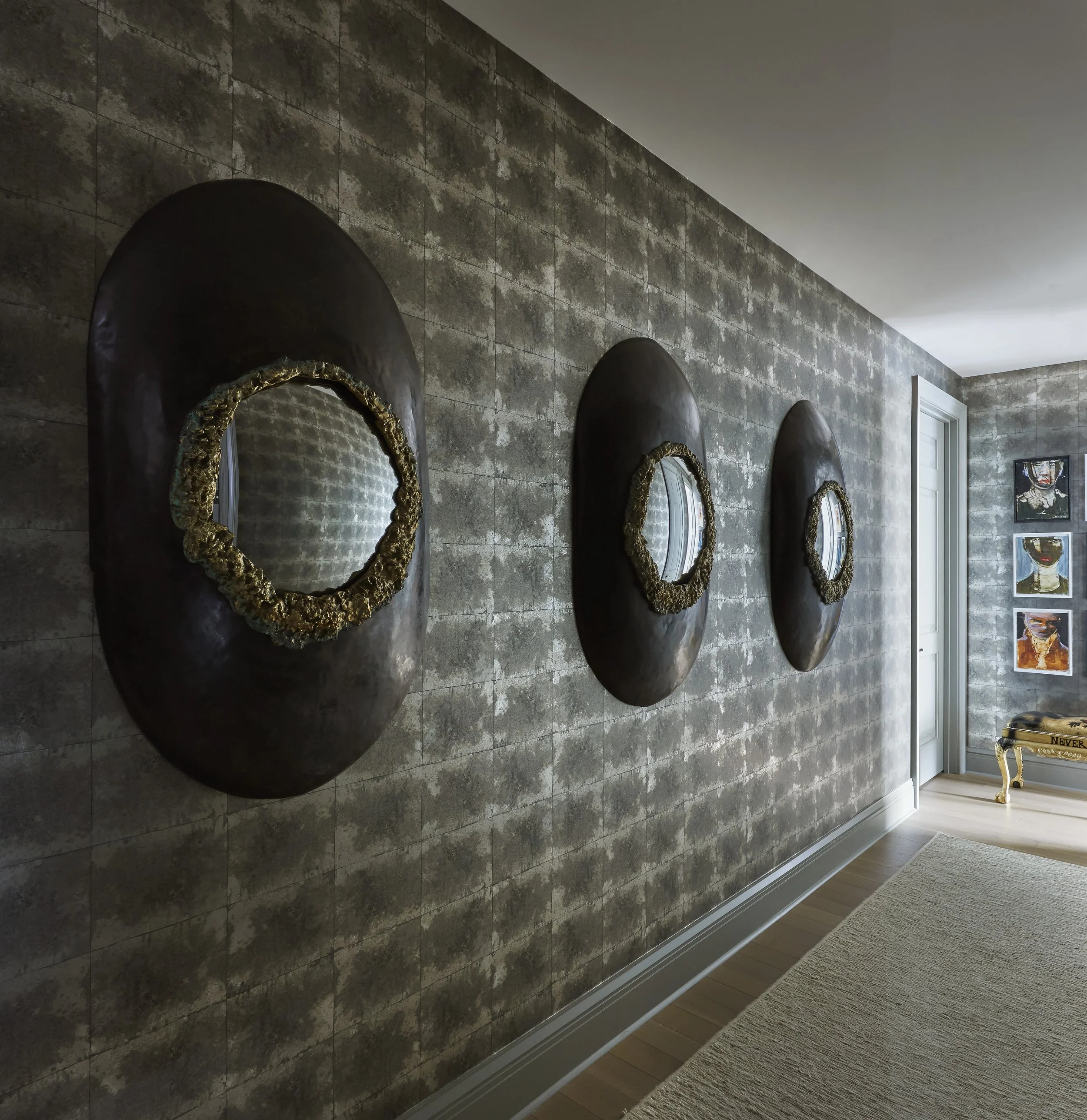 Interior of a modern living space with a stone tile wall adorned with round decorative mirrors with textured gold frames, a wooden floor, and a light-colored area rug near a window.