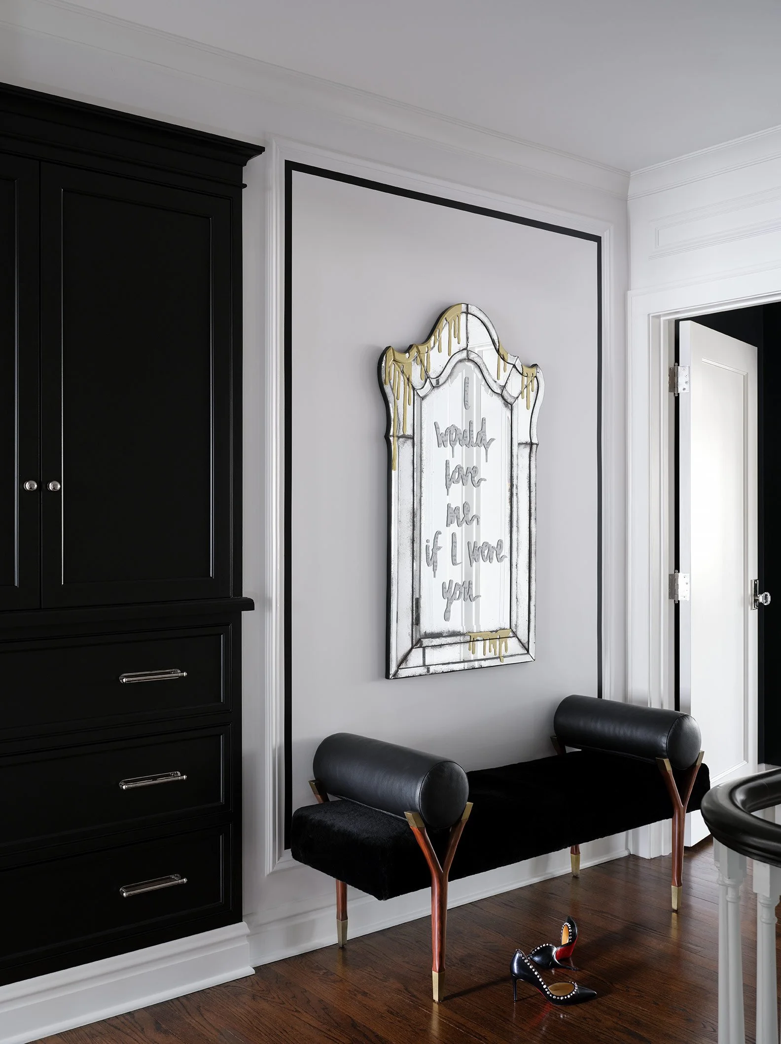 A modern interior with black furniture, a decorative mirror with gold accents, and a pair of black high heels with studs on the floor.