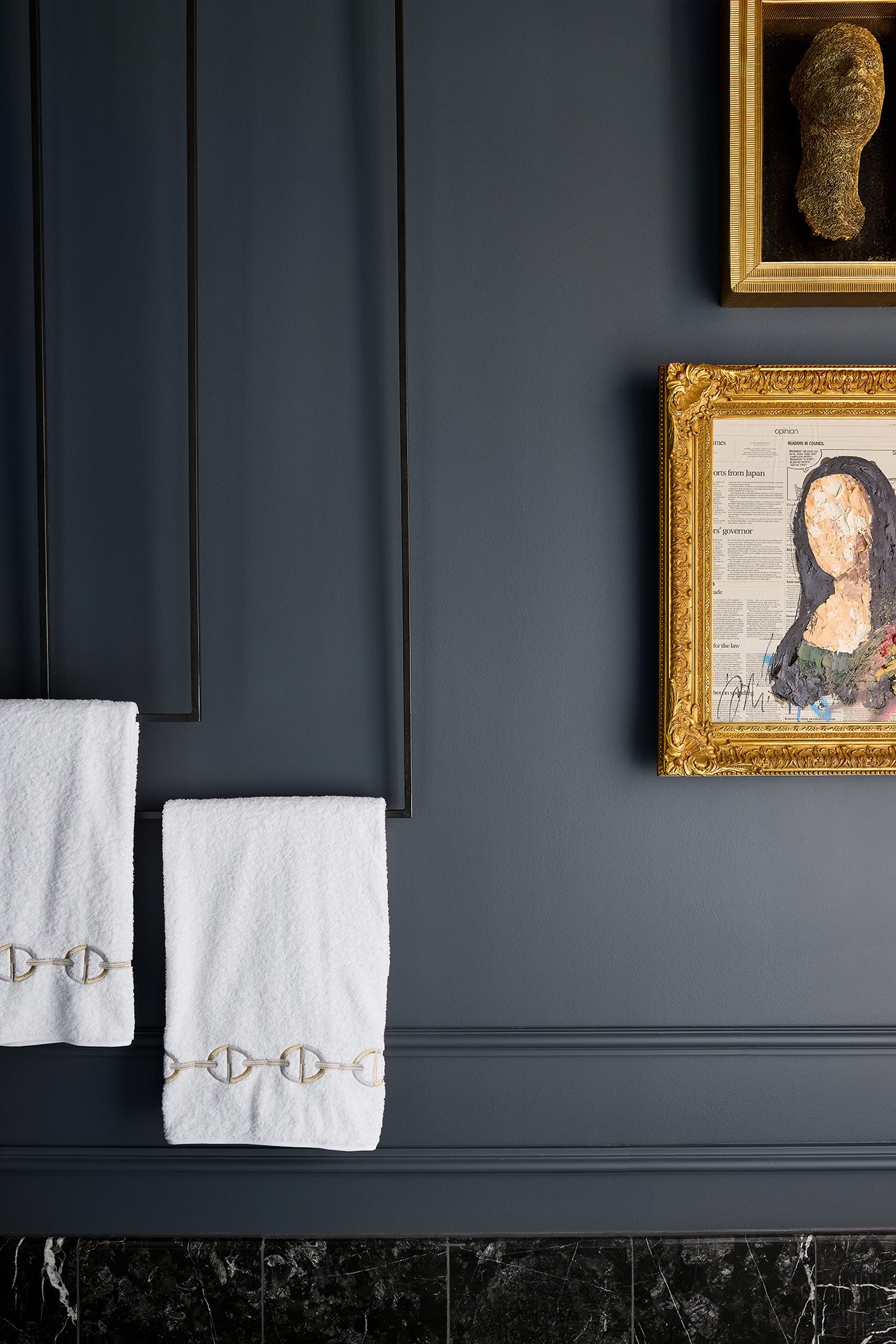 Interior view of a dark-colored wall with framed artwork and white towels hanging on a black rack.
