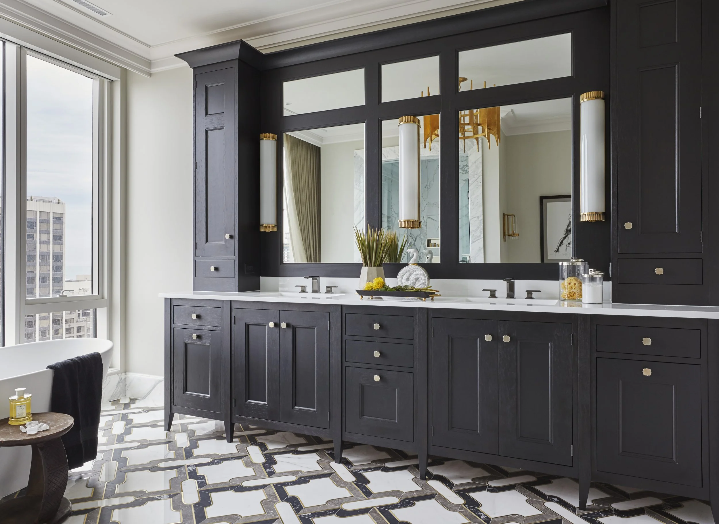 A modern bathroom featuring a dark navy blue vanity with multiple drawers and cabinets, topped with a white countertop. A large wall mirror extends across the vanity, with two elongated white and gold wall sconces mounted on each side. The room has a
