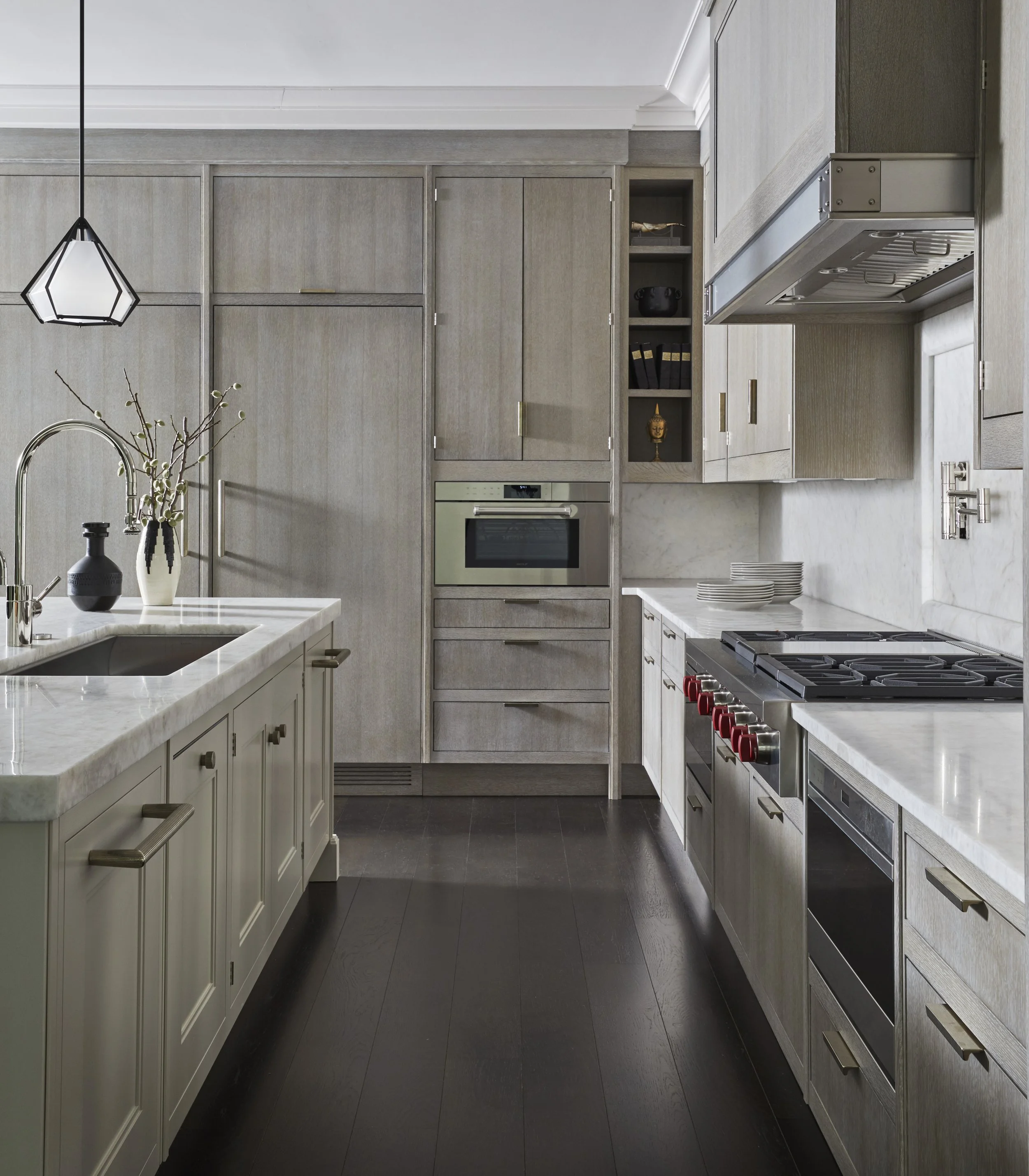 Modern kitchen with light wood cabinets, dark hardwood floor, marble countertop, built-in oven, stovetop with red knobs, and open shelving with decorative items.