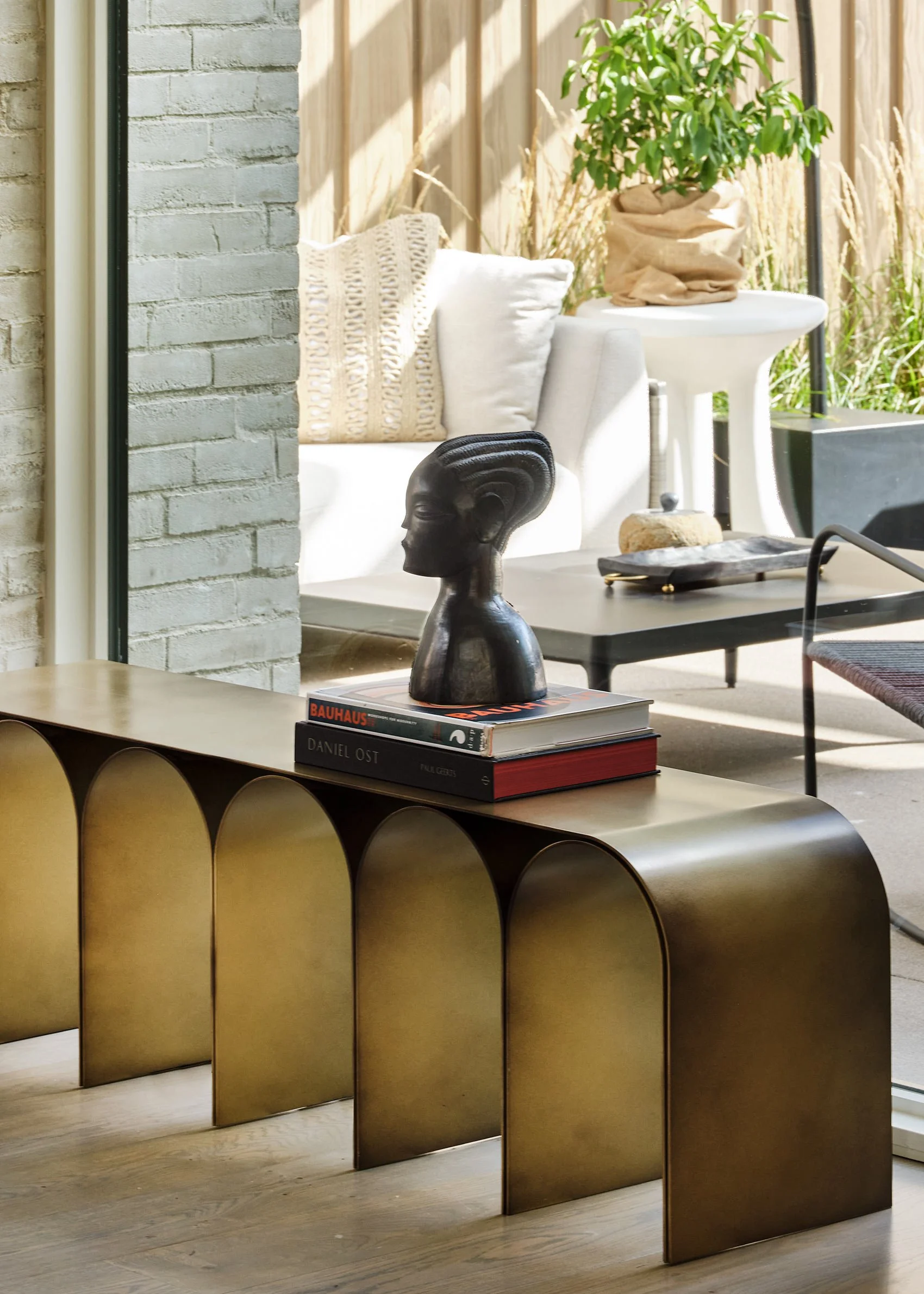 Interior space featuring a gold metallic curved object, books, a black bust sculpture, and a wooden floor.