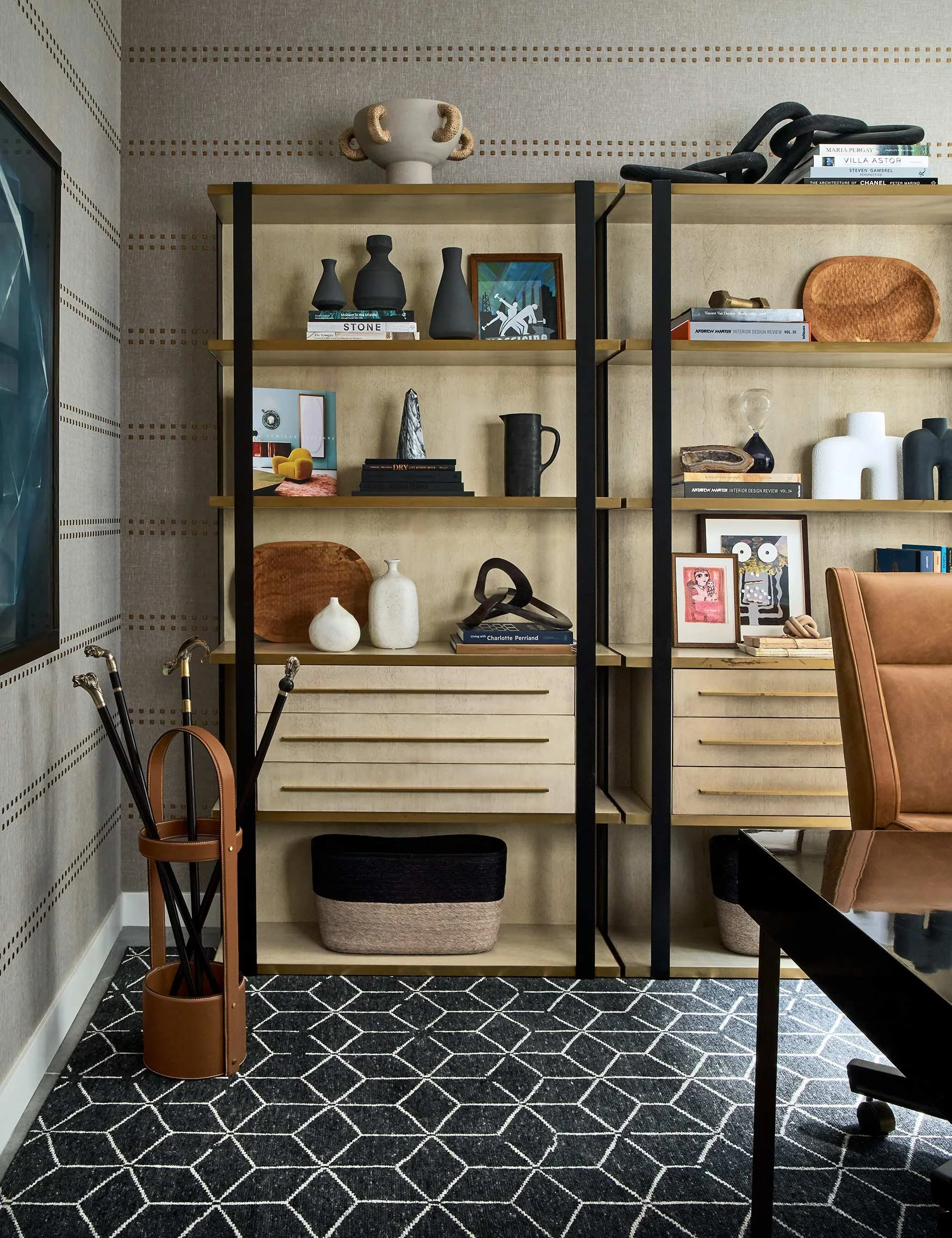 A modern shelving unit with various decorative objects such as vases, books, and artwork, set against a textured wall, with a patterned black and white rug on the floor.