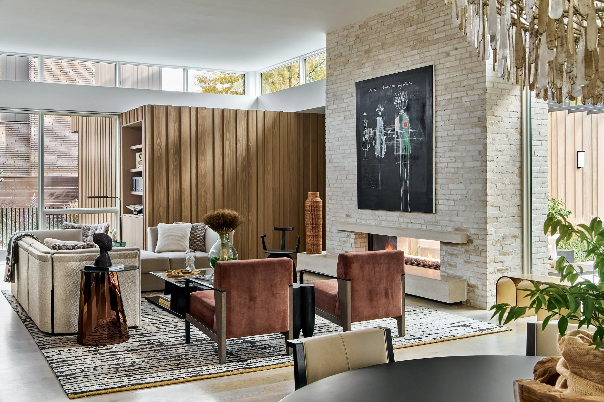 Bright living room with modern furniture, a fireplace, large windows, and a blackboard with sketches and writing on a brick wall.
