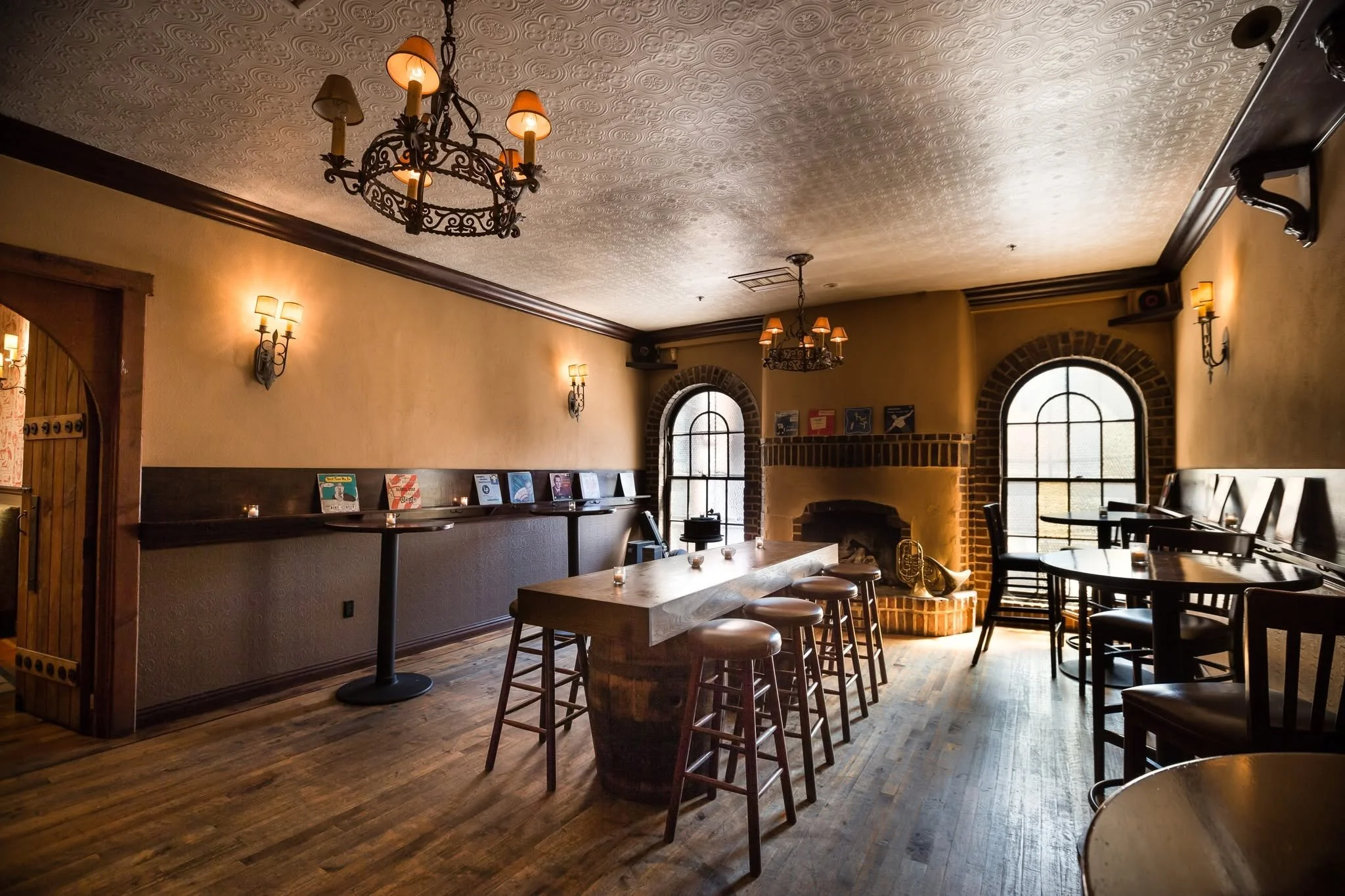 Interior of a cozy restaurant with wood floors, a fireplace, and large arched windows, decorated with warm lighting and vintage-style chandeliers.
