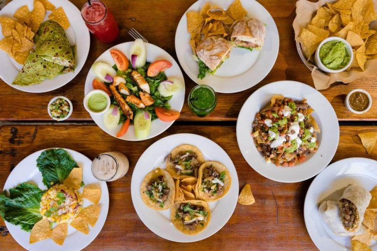 A variety of Mexican dishes including tacos, nachos, salad, and a dish with shredded meat, all on a wooden table.