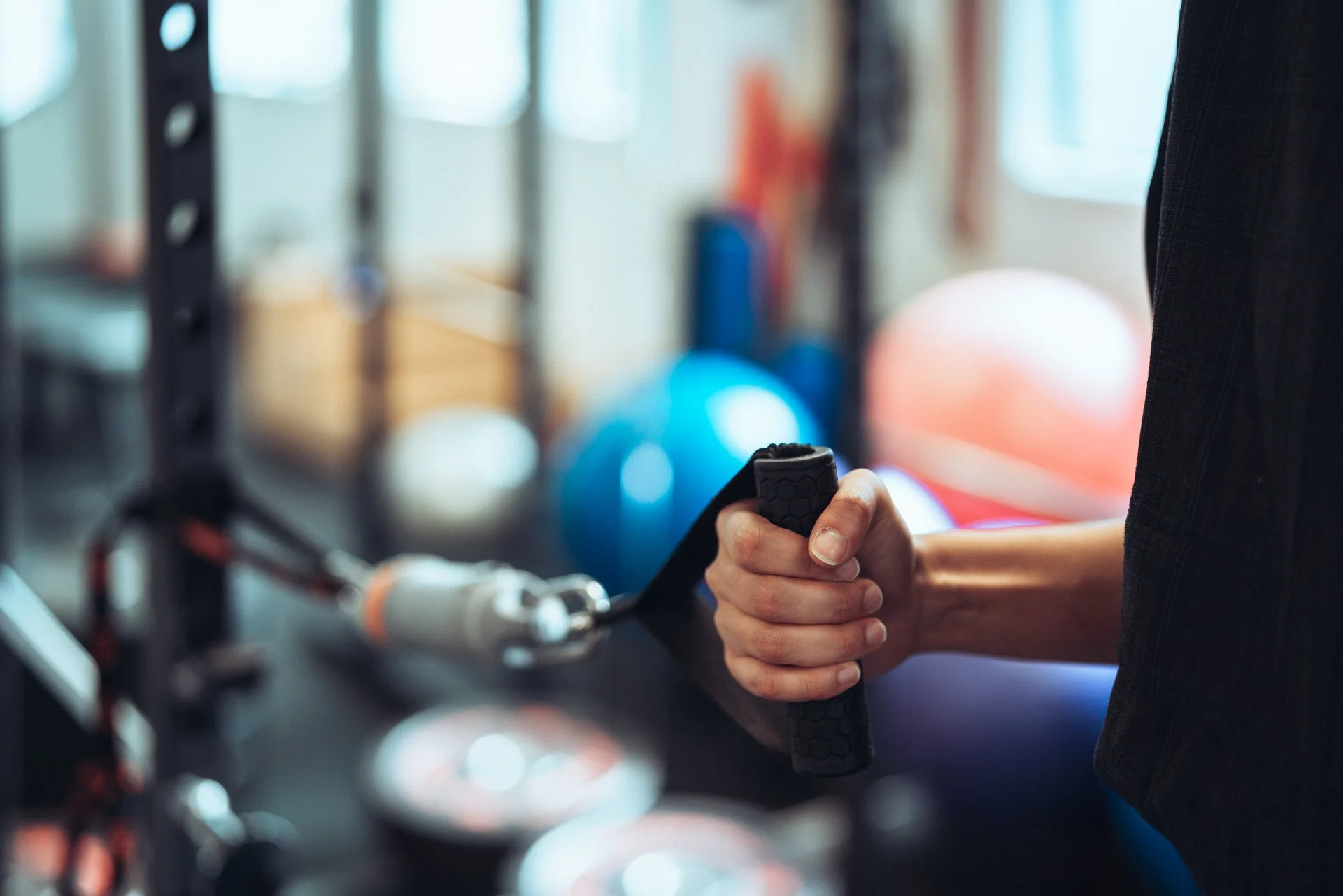 Close-up of a person gripping the handlebar of a treadmill in a gym, with blue and white exercise balls in the background.