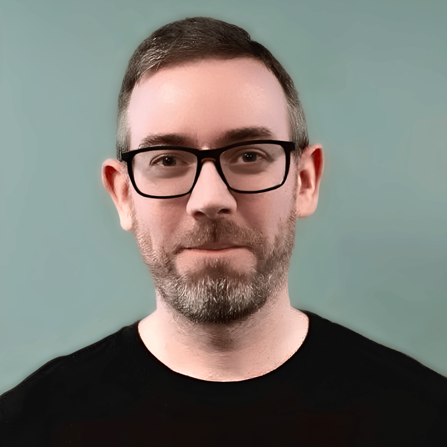 Portrait Photo of author Will Irvine facing the camera, wearing a black t-shirt and standing in front of a warm green coloured wall.
