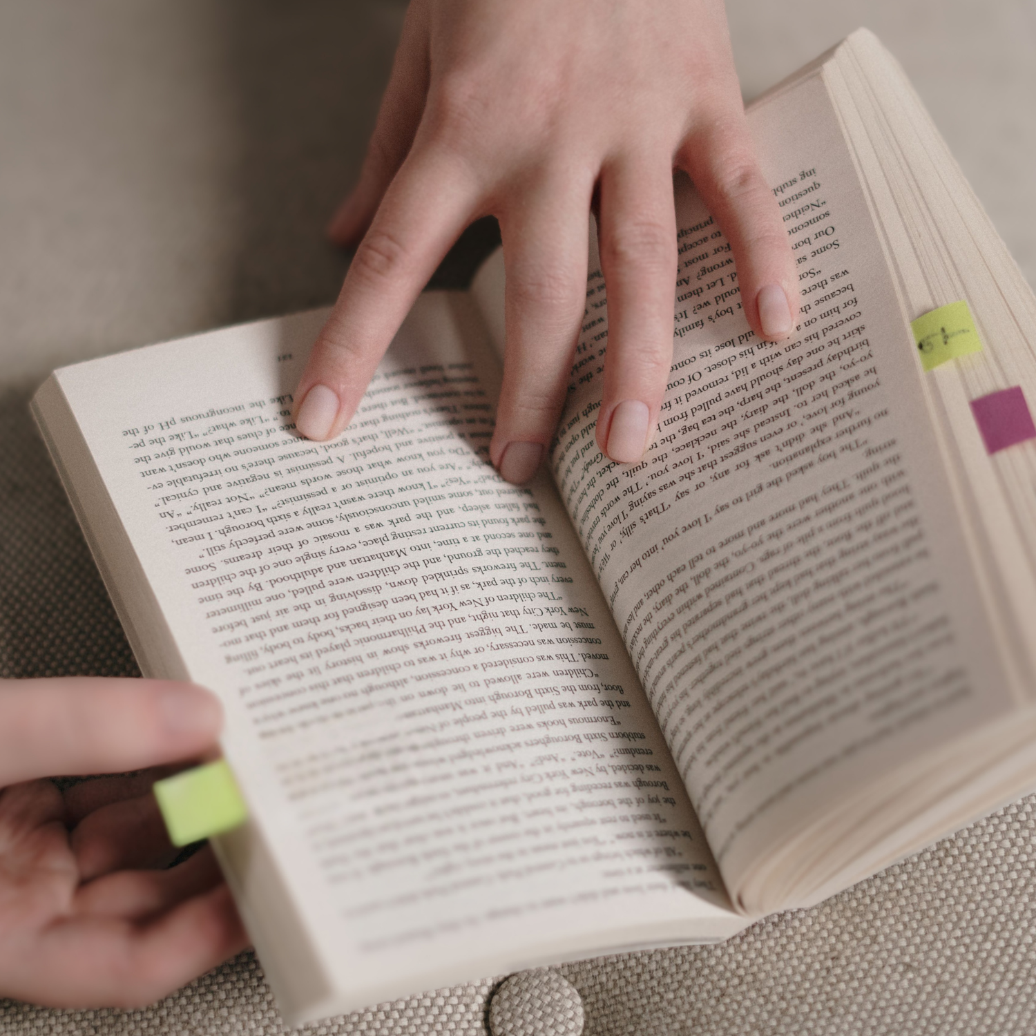 Photo of an book with coloured sticky notes lining the edge of several pages as a pair of hands from a beta reader hold the book open for review.