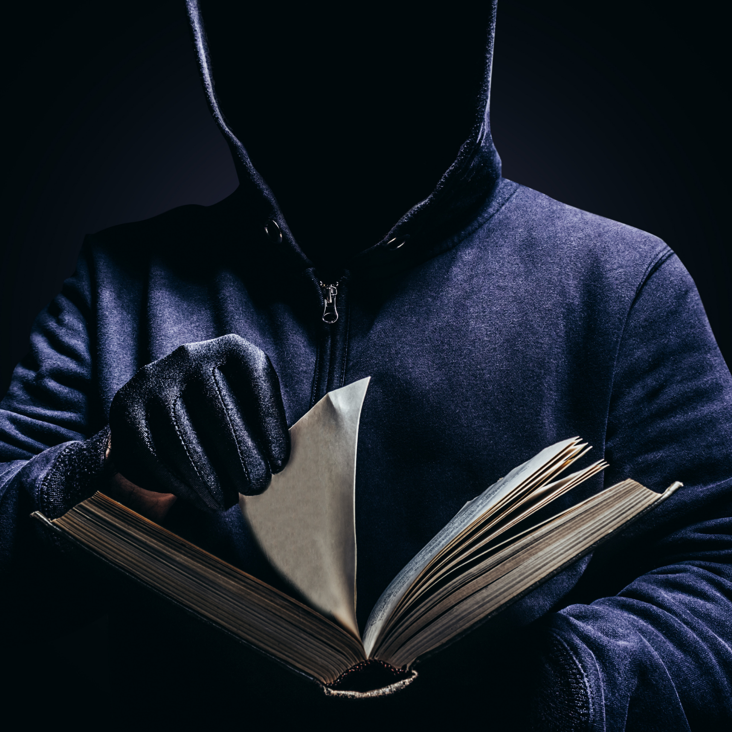 A dark photo with a black background depicting a thief in a black hoodie, wearing black gloves, turning the pages of a book they intend to steal.