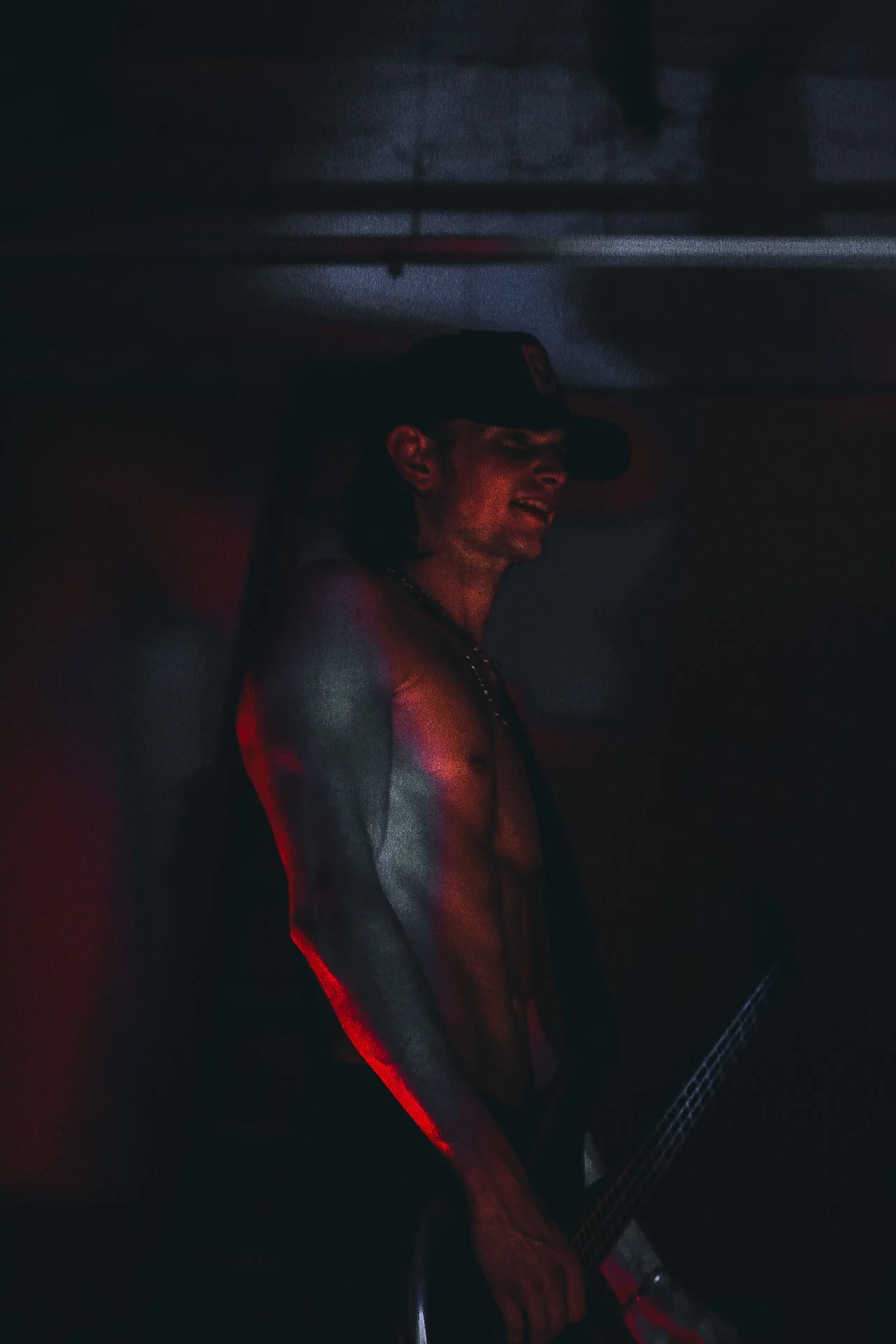 Person playing a guitar in a dimly lit room, illuminated by red and blue lighting.
