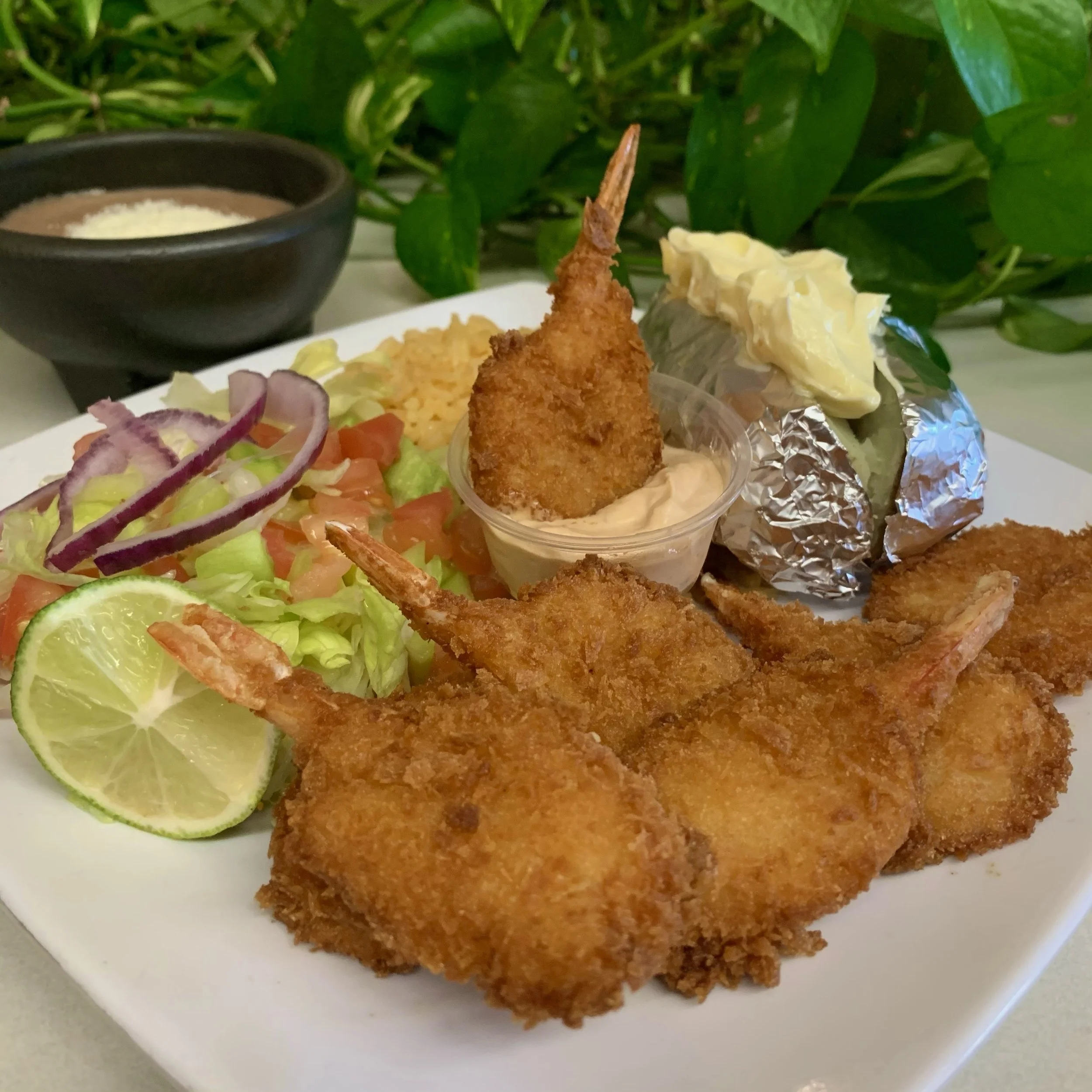 Crispy fried shrimp served on a plate with lime slices and a side of salad, with a bowl of dipping sauce in the background.