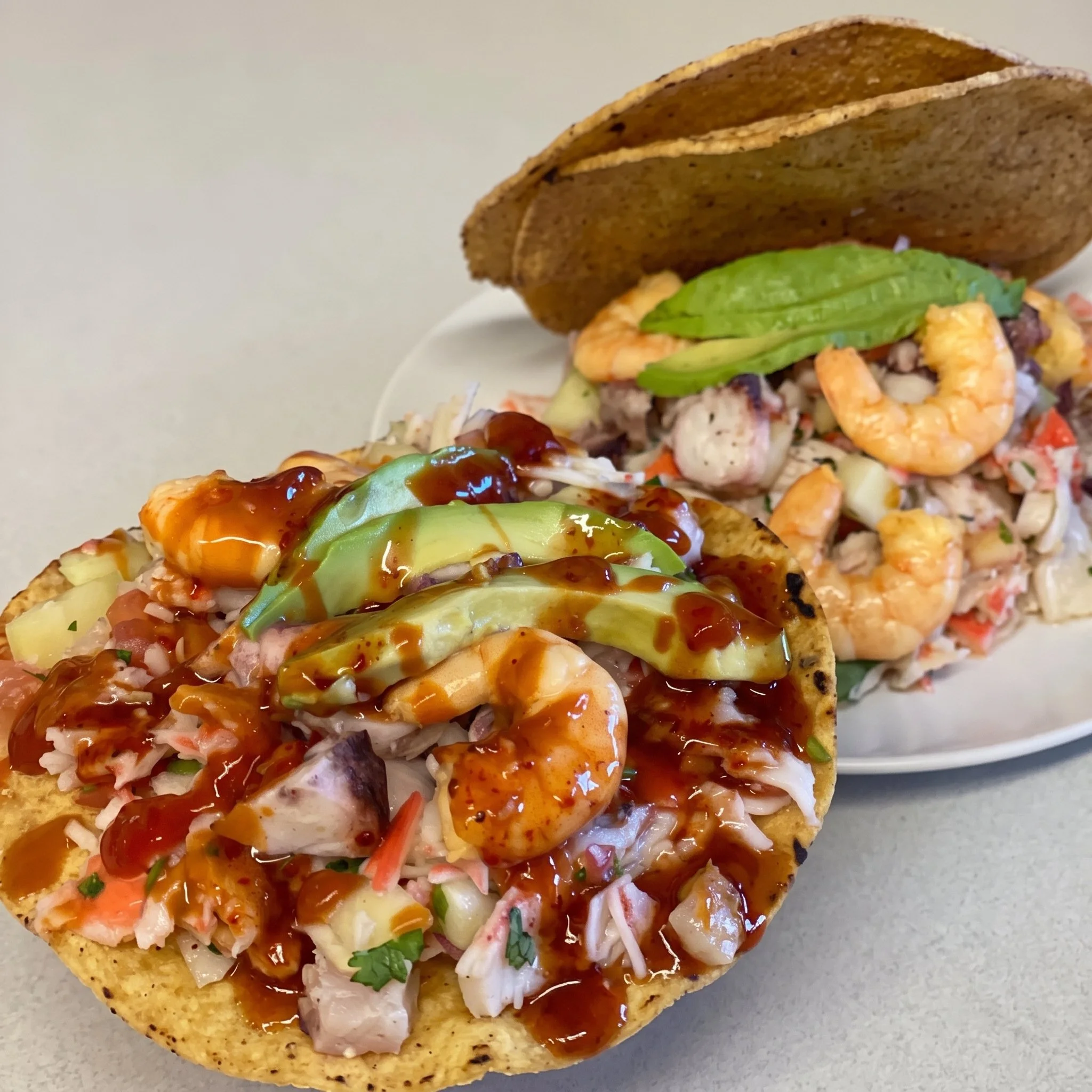 Close-up of a loaded taco with shredded lettuce, diced tomatoes, diced onions, shredded cheese, shrimp, and barbecue sauce in a hard taco shell.