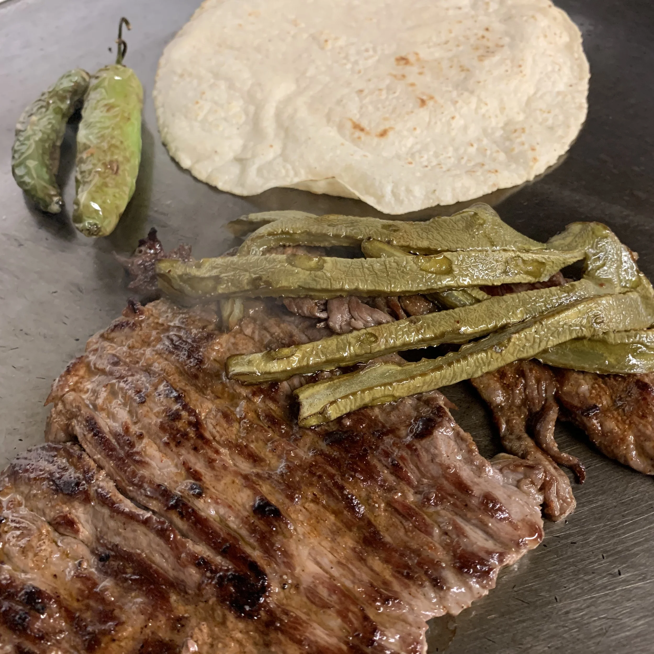 Close-up of a grilled steak topped with pickled jalapeño peppers on a black surface.