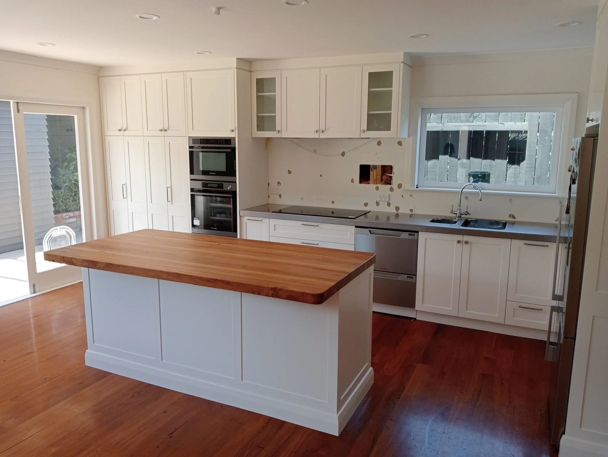 Kitchen with white cabinets, a central island with a wooden countertop, stainless steel appliances, and a window overlooking the backyard.