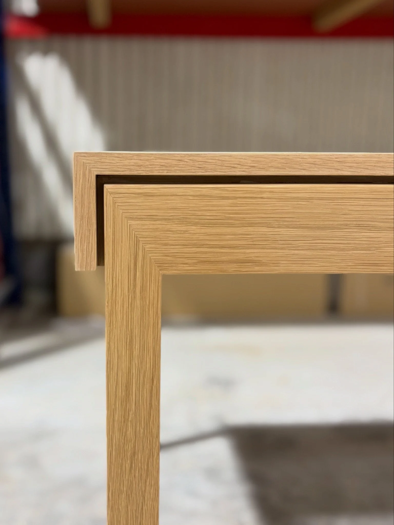 Close-up of a wooden table leg against a background of a gray wall and blurred objects.