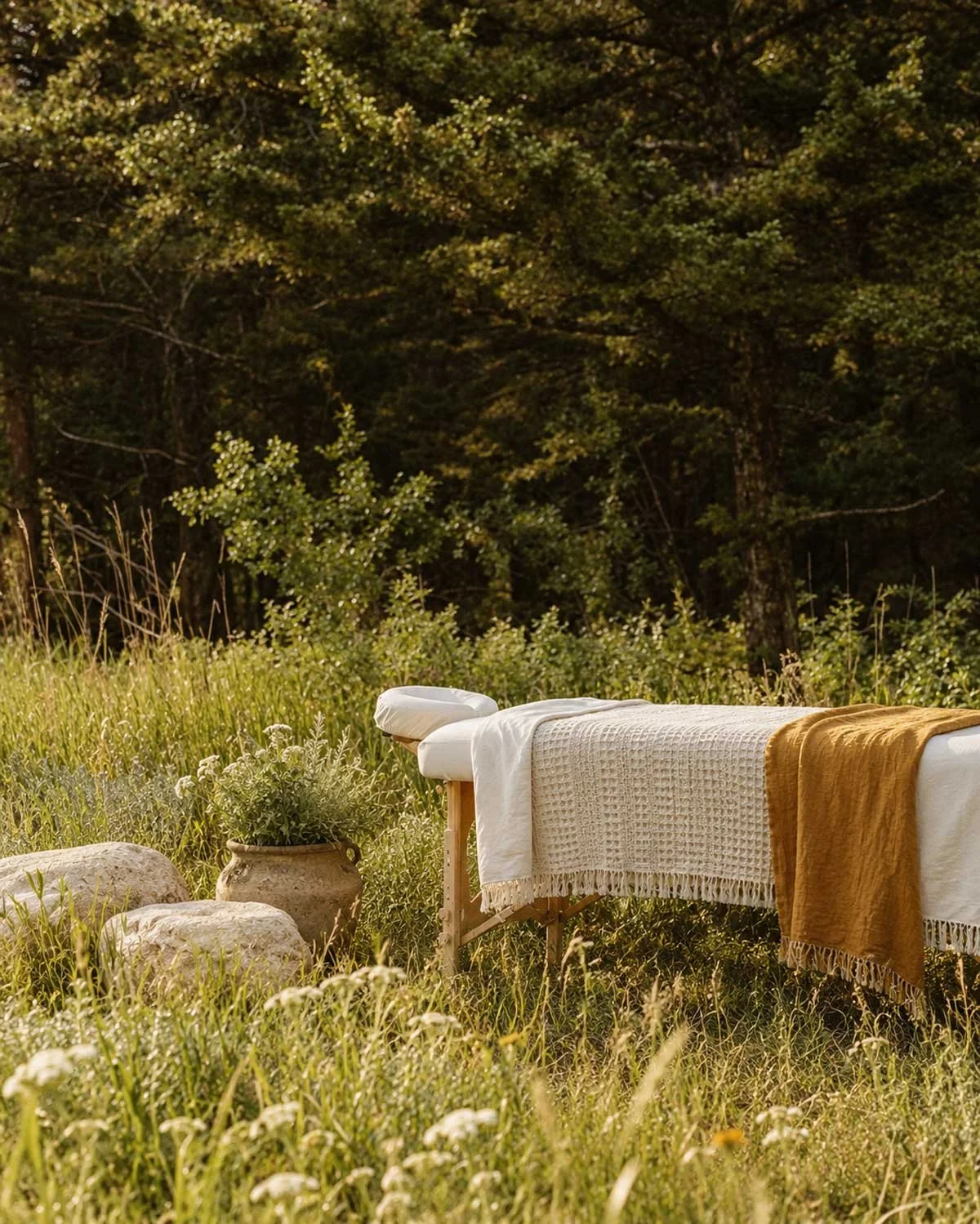 Outdoor massage table covered with white and yellow towels set in a grassy field with trees in the background.