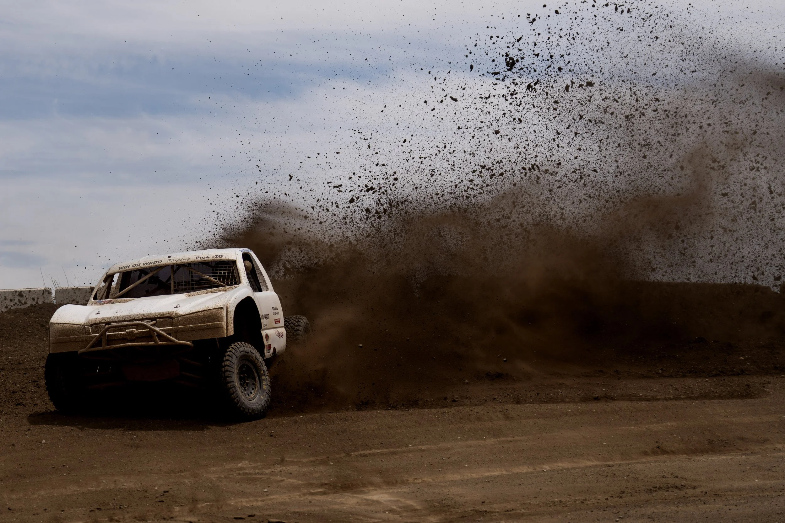 An off-road pickup truck kicking up dirt and dust as it races on a dirt track during a race or rally.