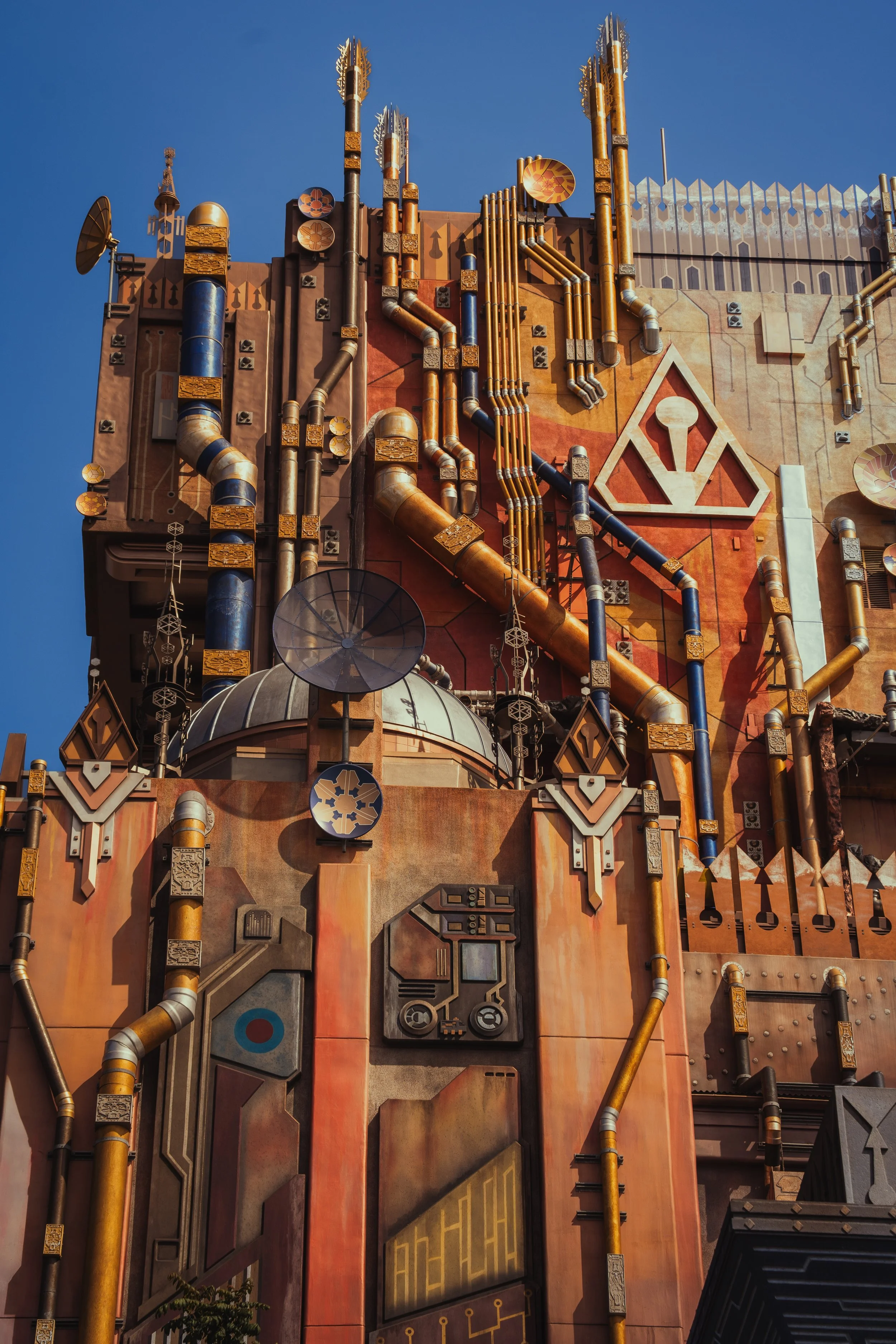 A tall building styled like a spaceship or sci-fi structure with various pipes, antennas, and geometric decorations against a clear blue sky.