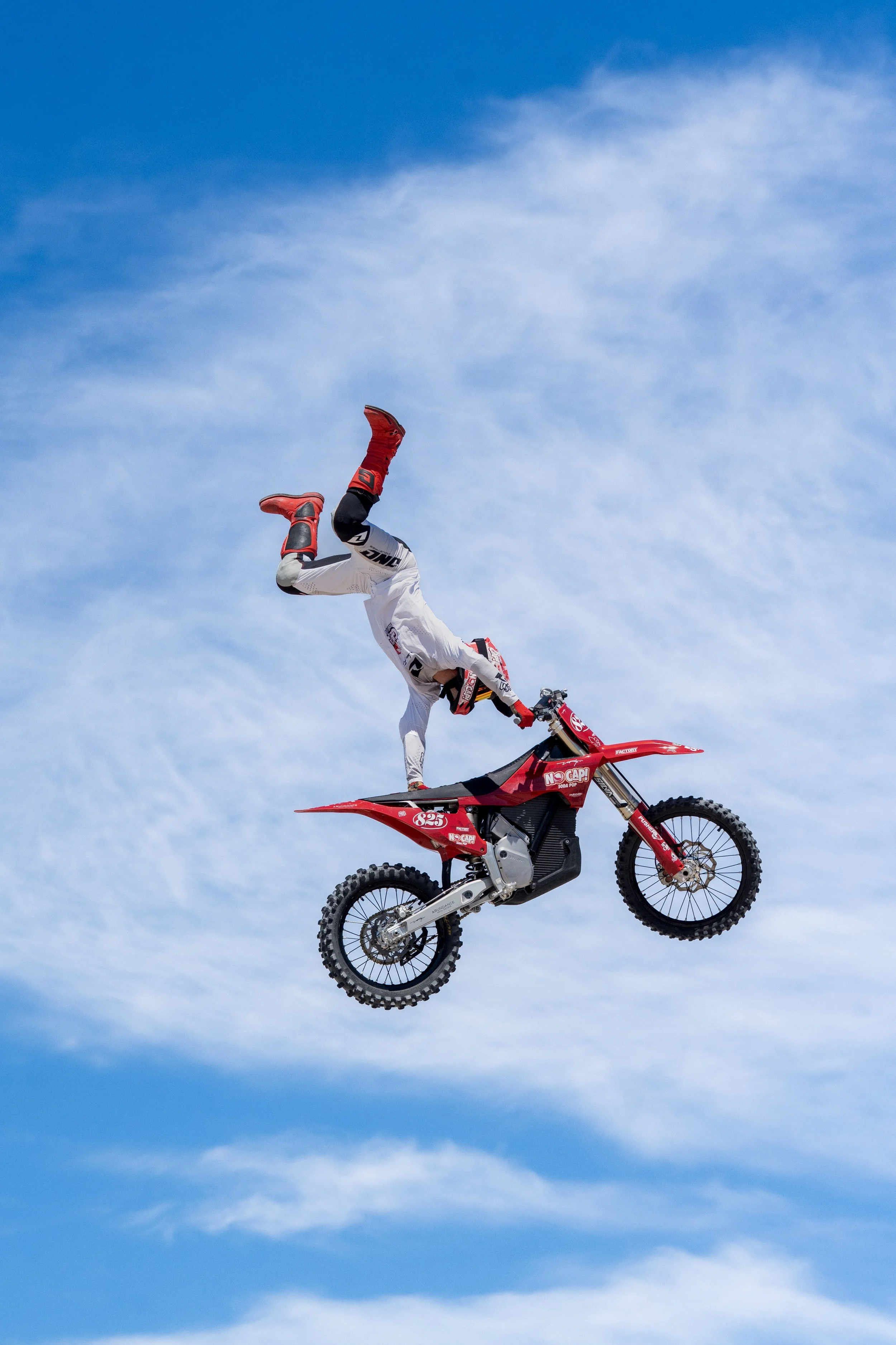 Motocross rider performing a mid-air stunt on a red dirt bike against a blue sky background.