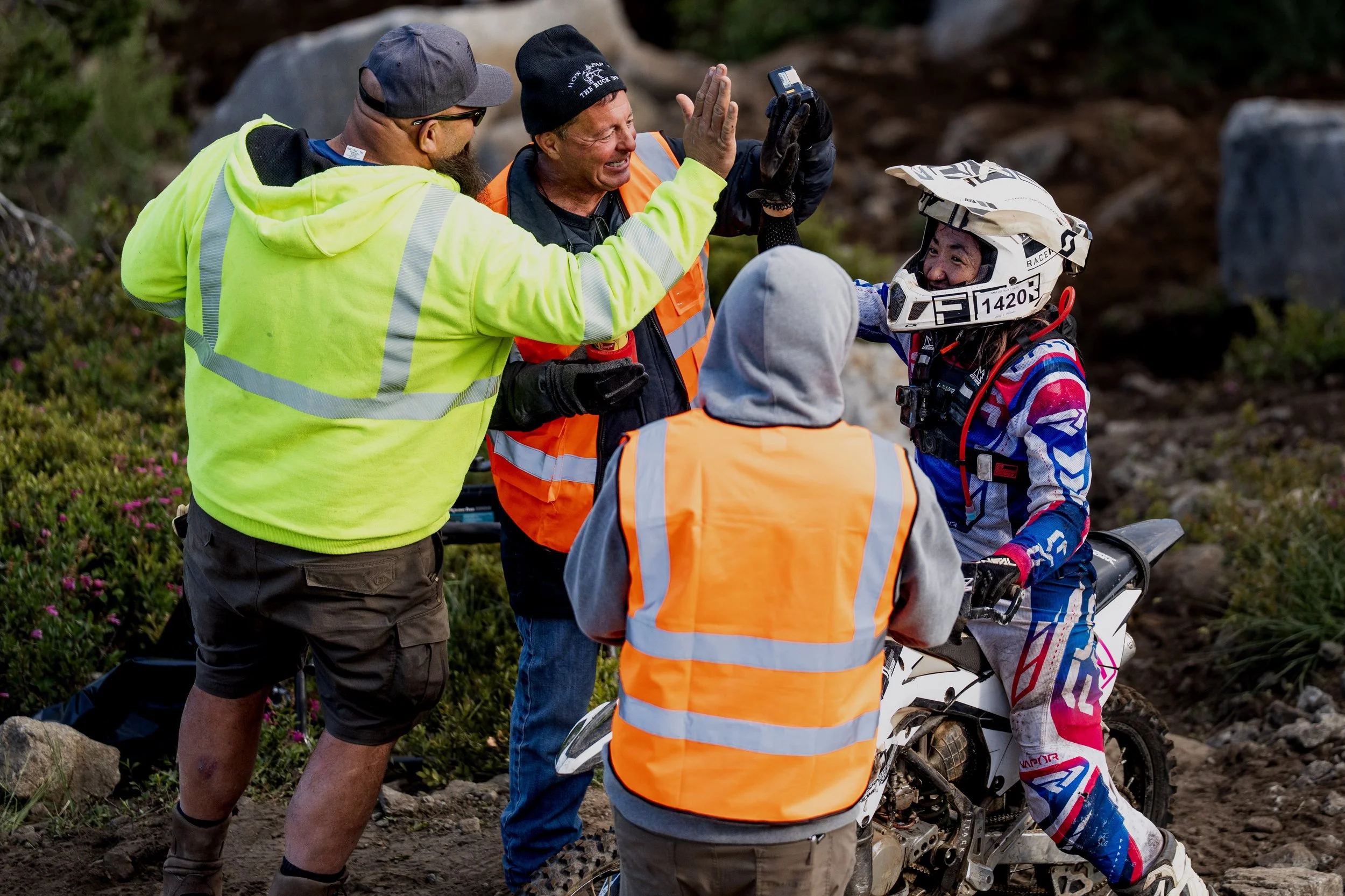 A group of people, including a motocross rider wearing a full helmet and gear, are receiving assistance from responders in bright clothing near a dirt trail.