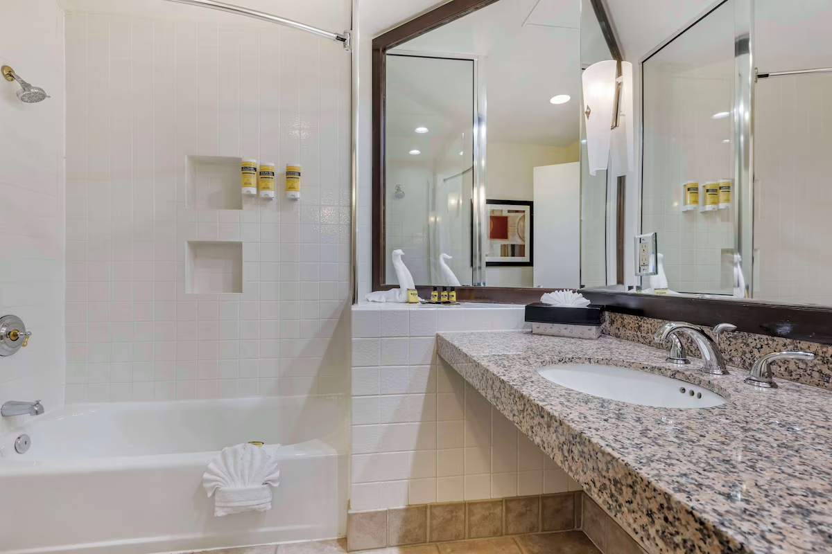 Bathroom with a granite countertop sink, a large wall mirror, a lamp, and a bathtub with a folded towel shaped like a fan.