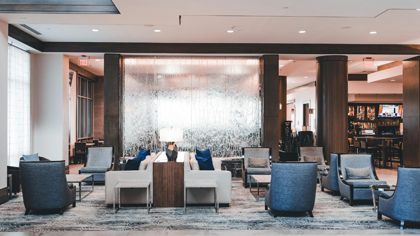 Modern hotel lobby with chairs, sofas, a central table, and a decorative glass partition.