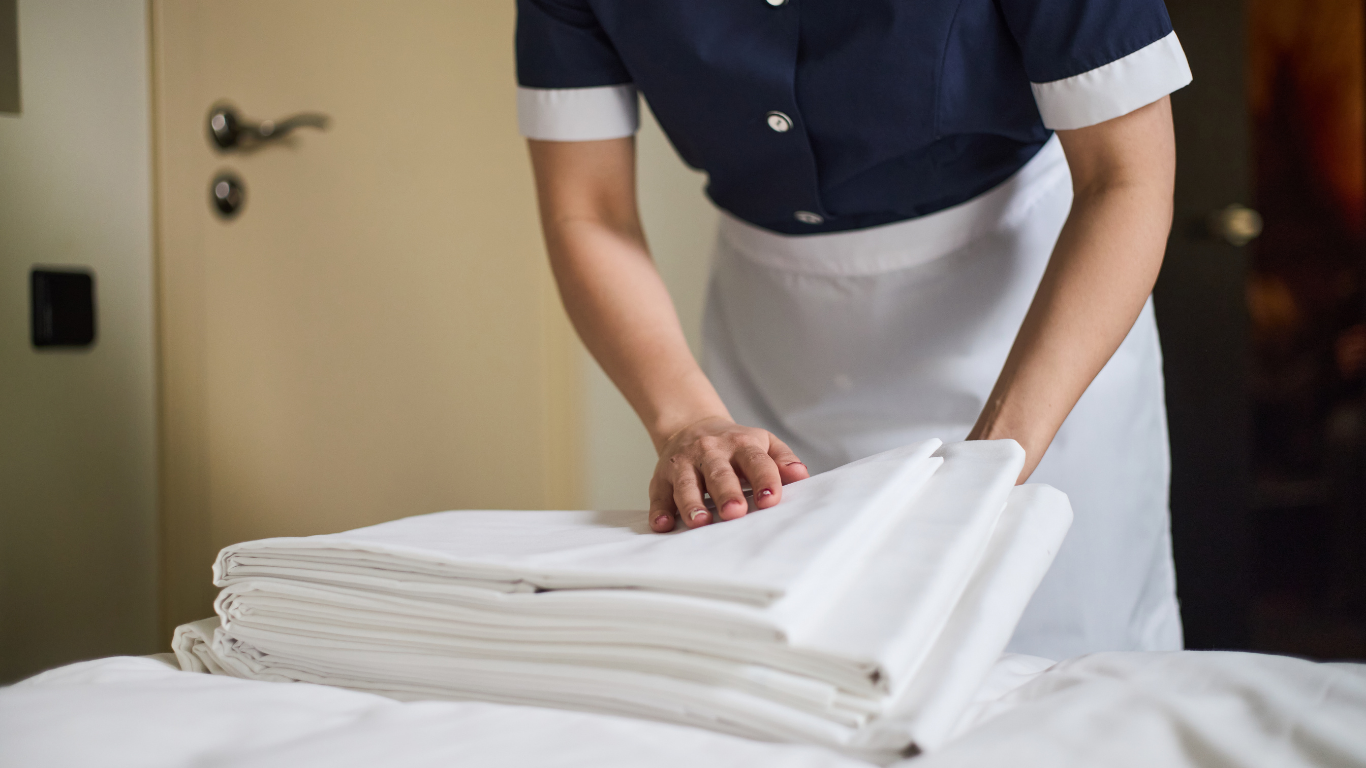 A person in a blue and white uniform folding linens on a bed.