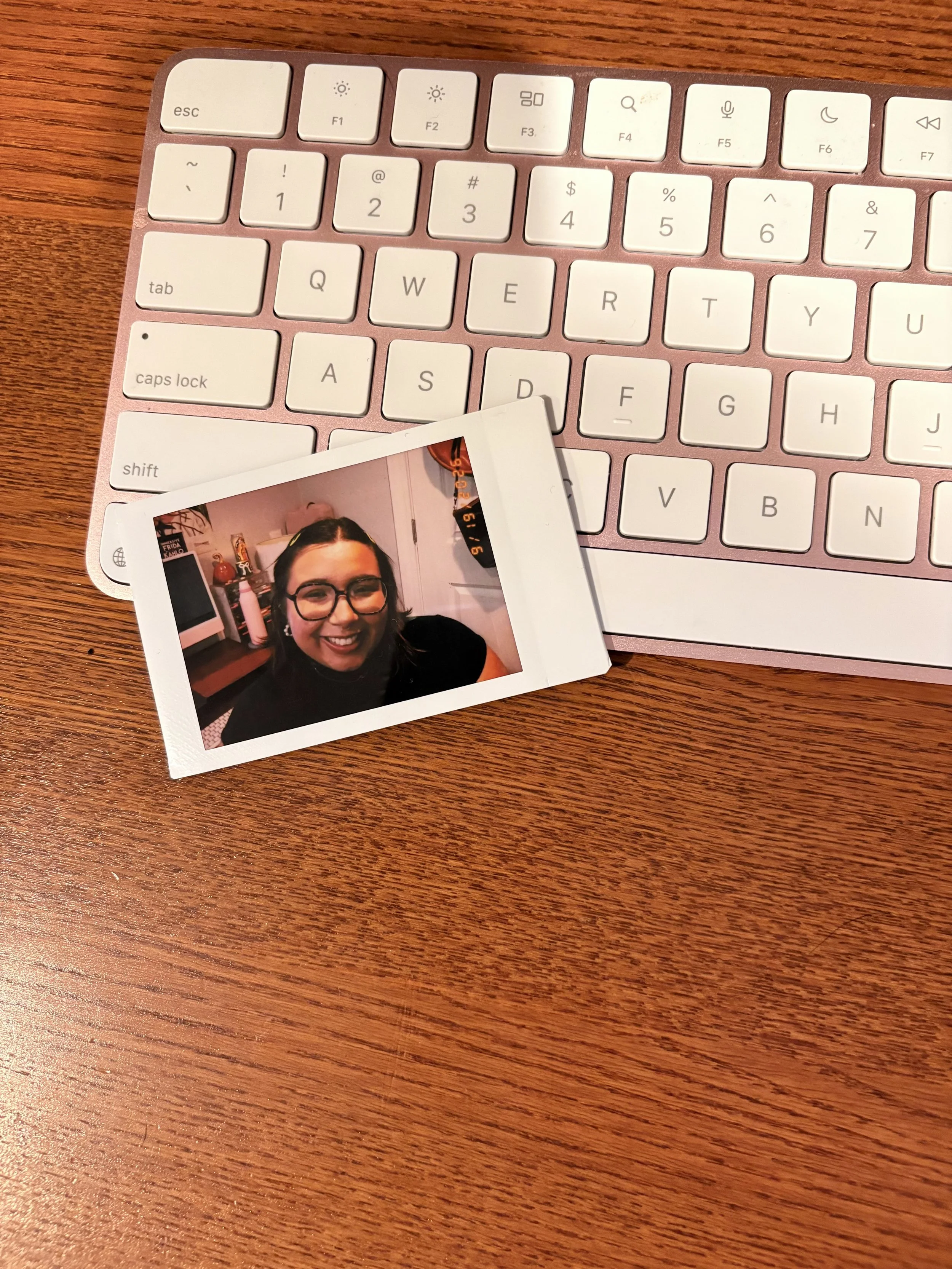 A close-up of a pink computer keyboard with a printed photograph of a smiling woman with glasses and dark hair resting on the keyboard.