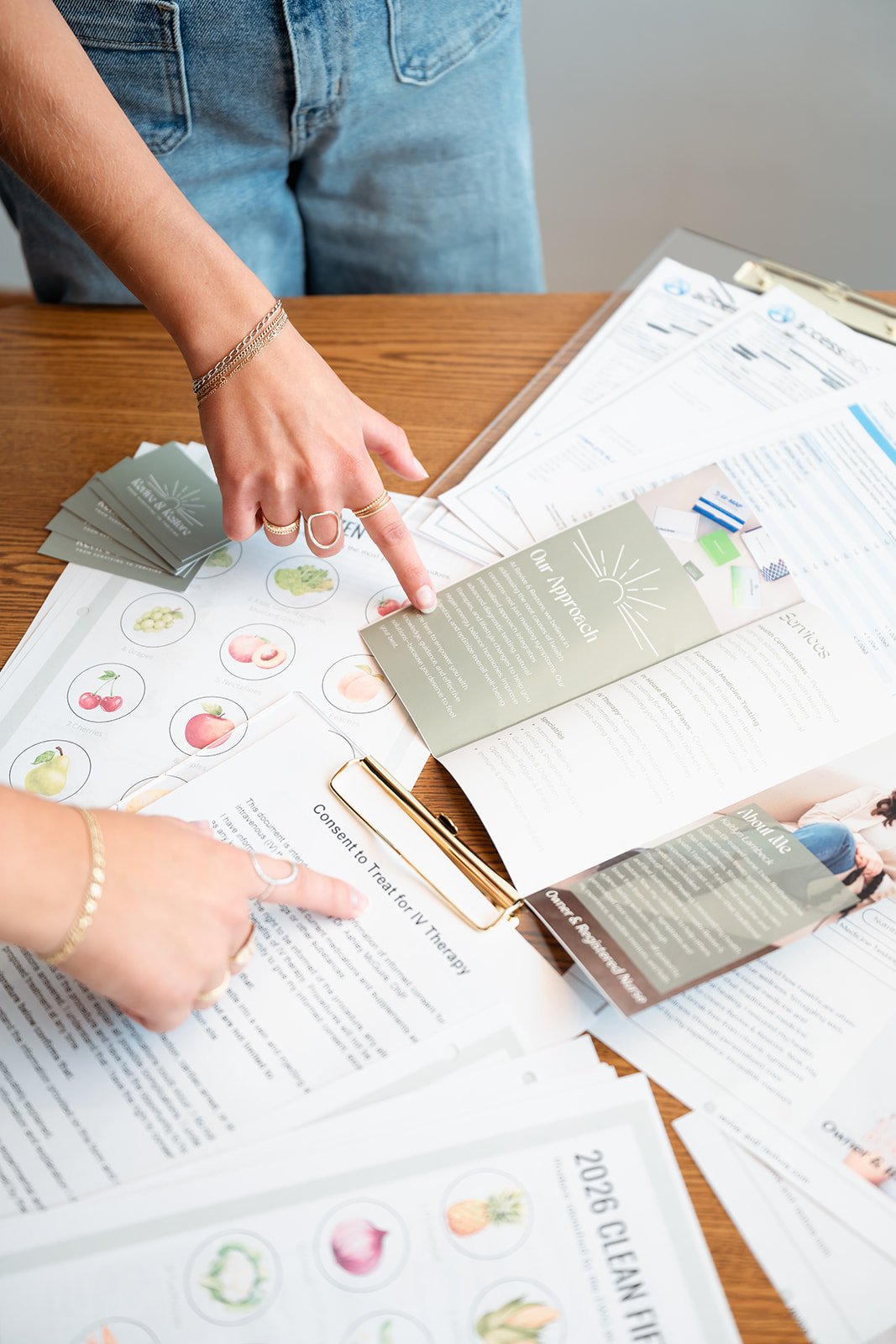 Person pointing to informational pamphlet about fruits on a desk with various papers and brochures.