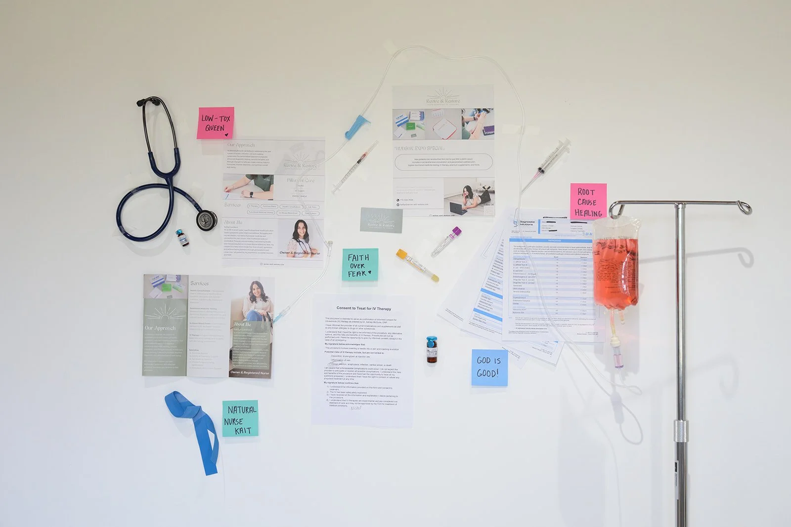Medical bulletin board with papers, medication, and medical tools attached, including a stethoscope, IV fluids, and signs with words like 'Low-Tox Queen' and 'Root Cause Healing'.