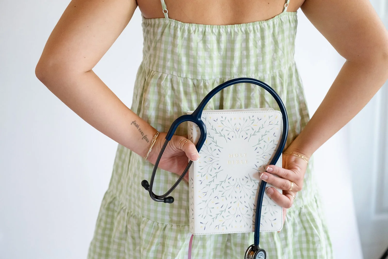 A woman in a green and white checkered dress holding a Holy Bible and wearing a stethoscope.