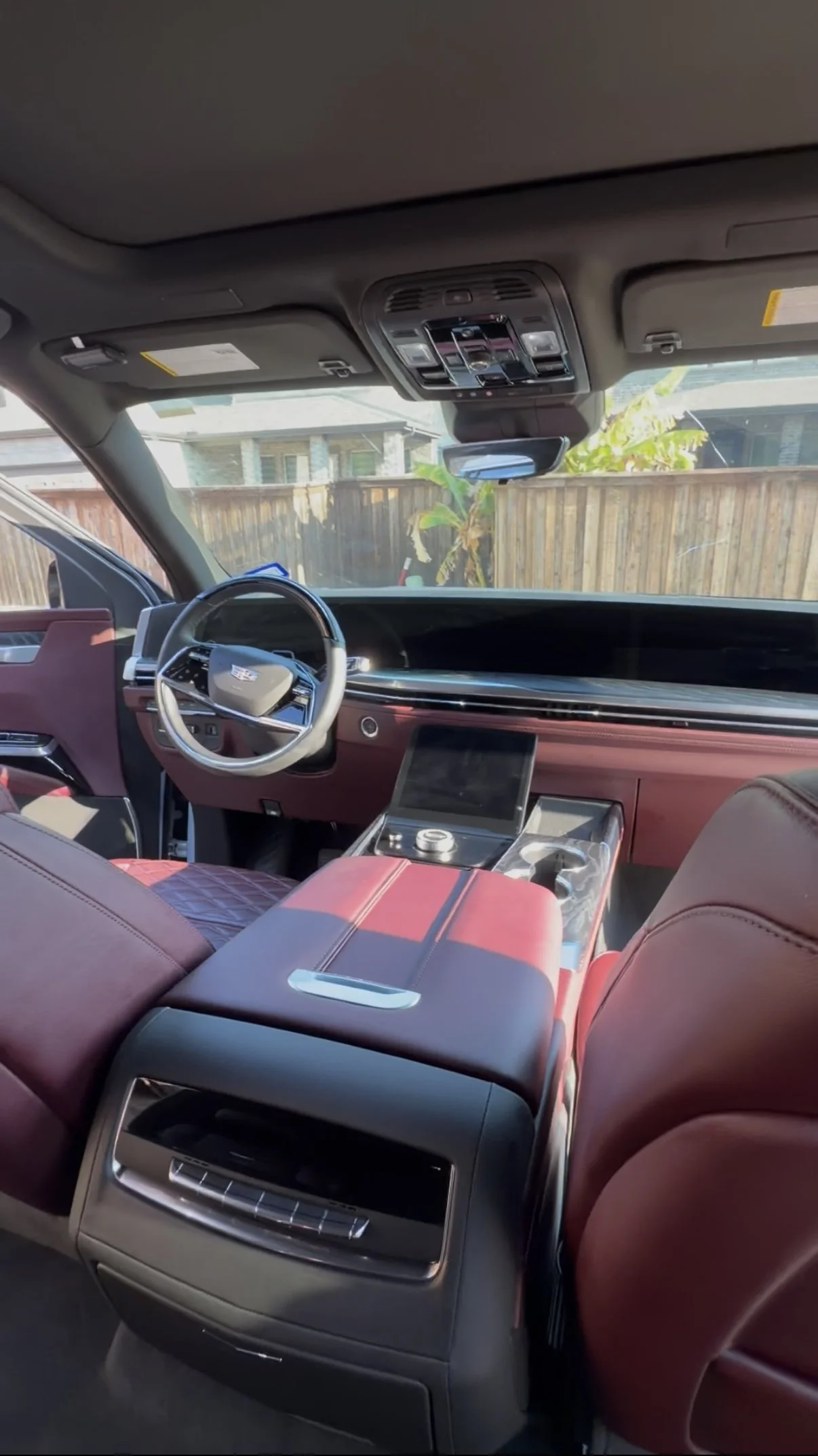 Interior of a modern vehicle with a red leather seat, dashboard, and center console, viewed from the back seat, with a view outdoors through the windshield and sunroof.