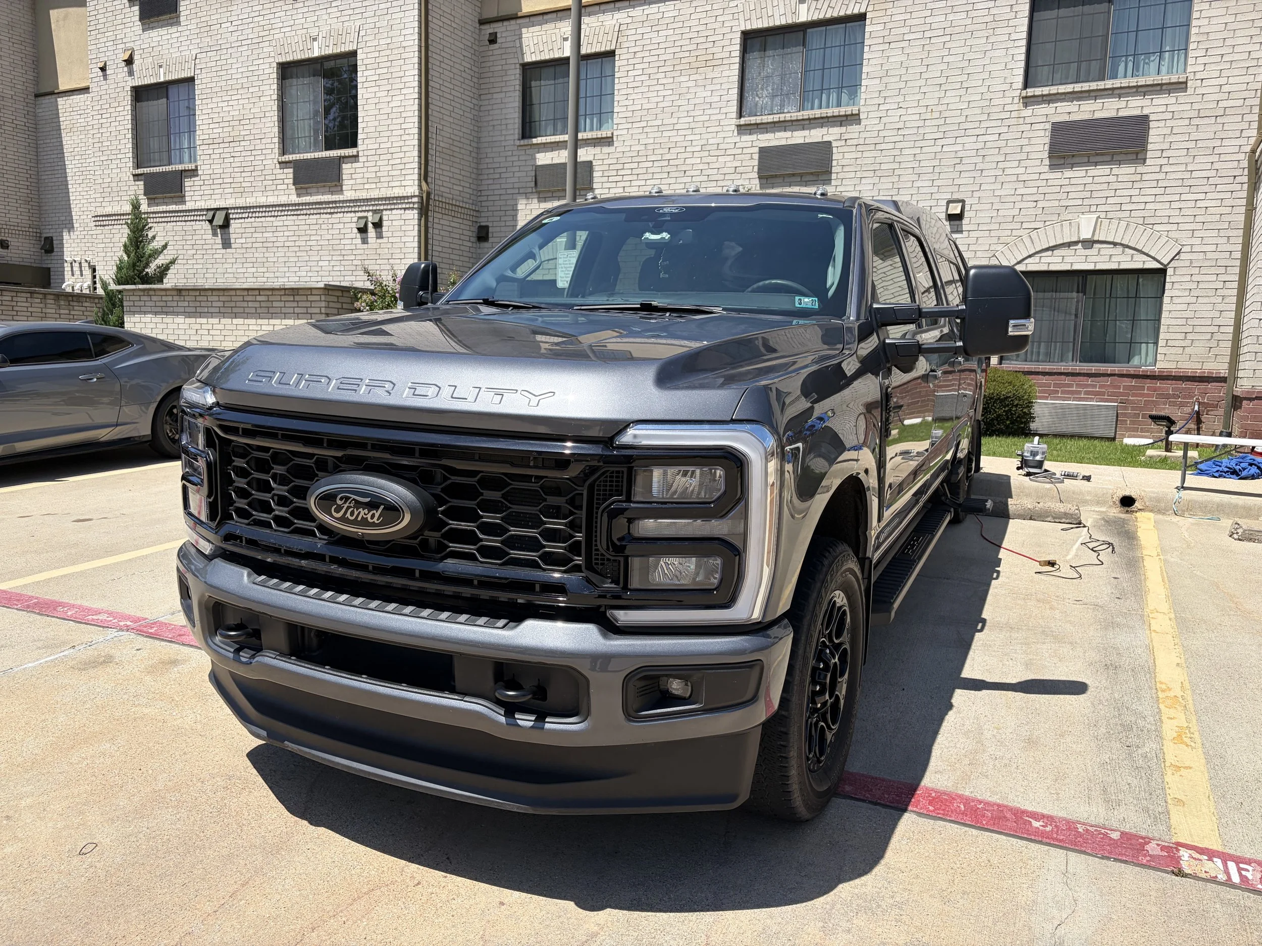 A black Ford Super Duty truck parked in a parking lot in front of a beige brick building.