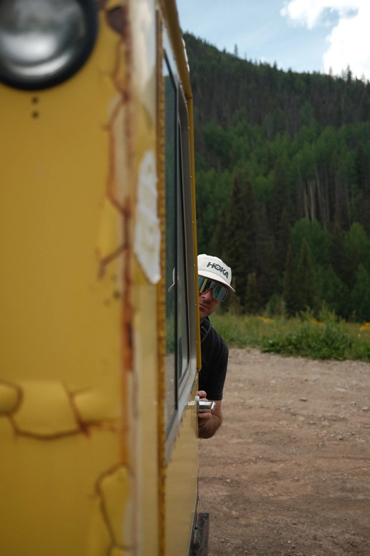 Phil Henderson on location, seen past the side of a yellow vehicle in the mountains