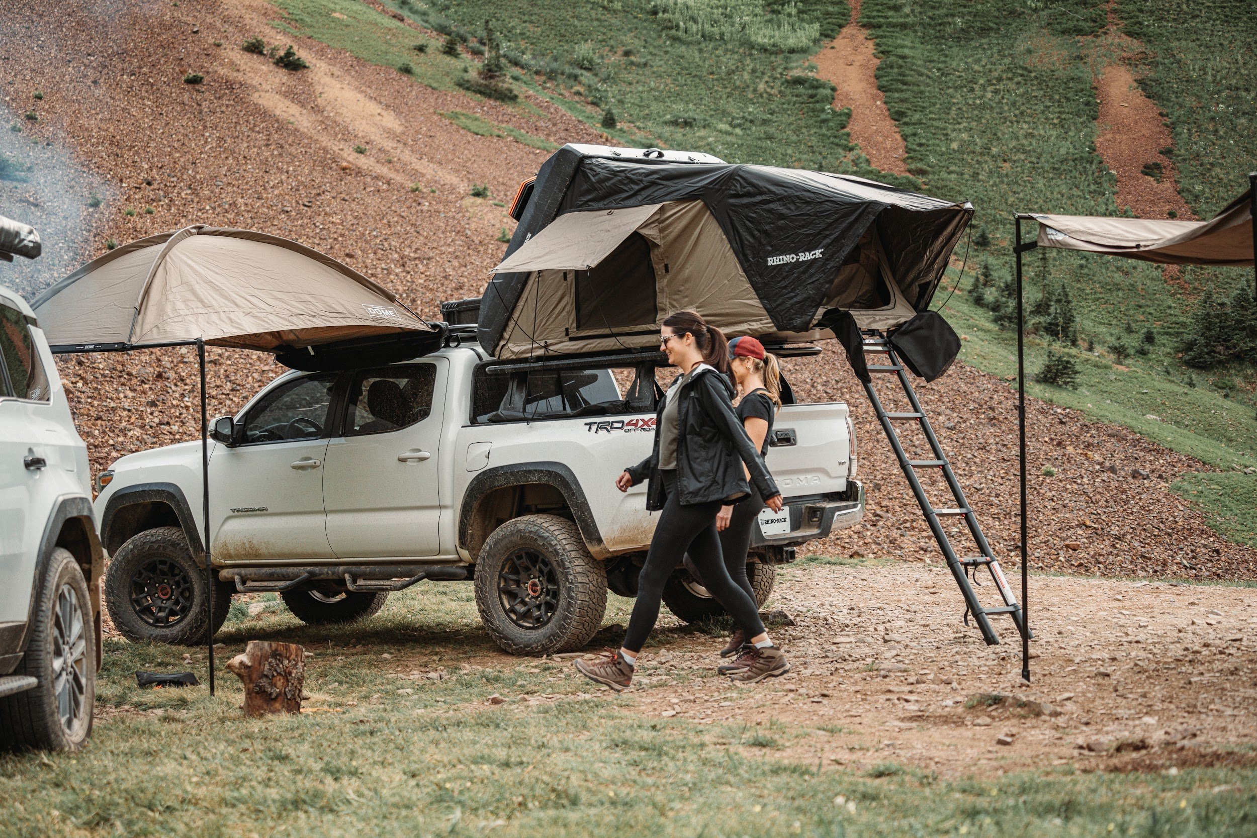 Camp in the mountains: Tacoma with a Rhino-Rack rooftop tent, ladder and awnings, two women walking by.