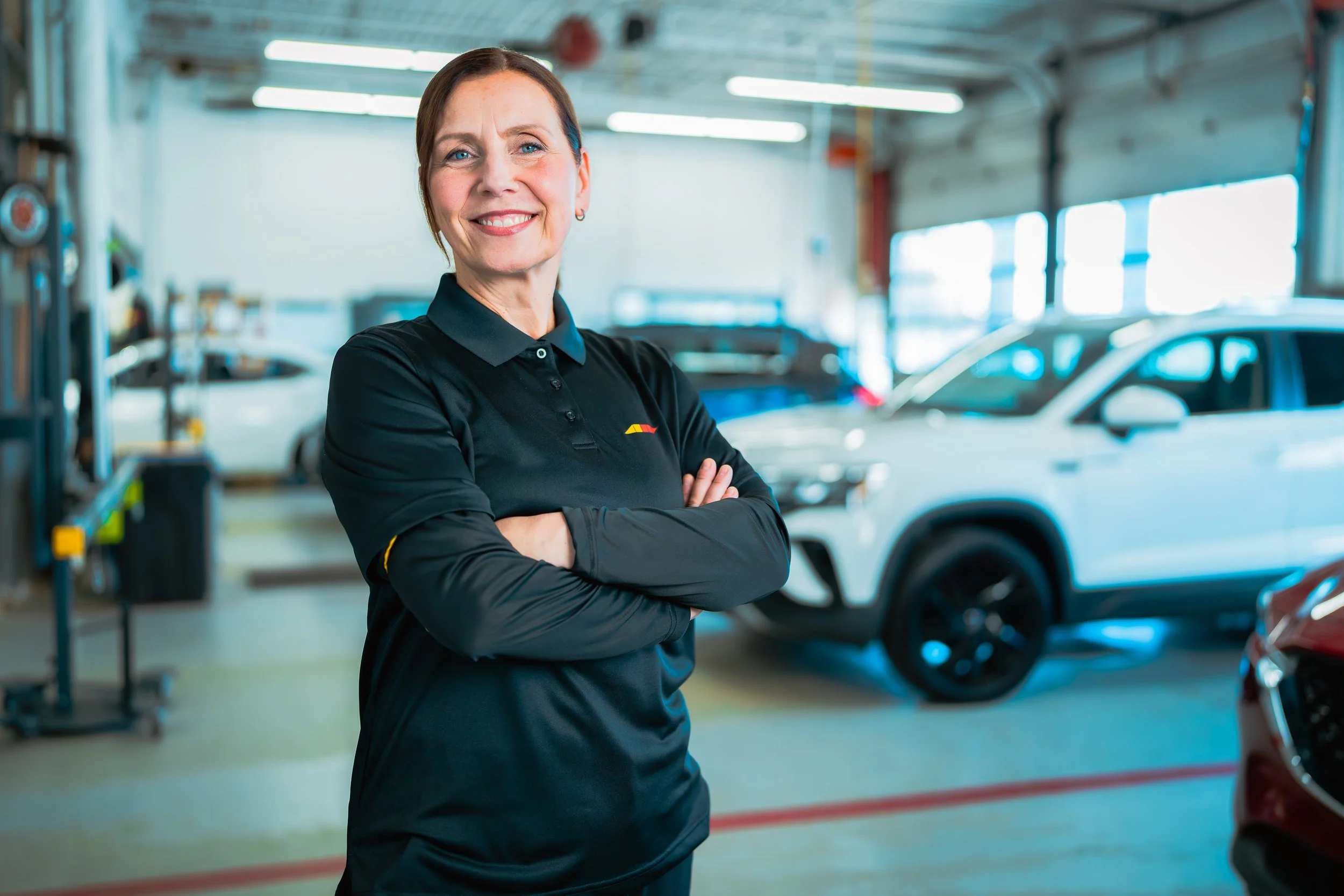 Lebeau Vitres d'auto technician, arms crossed, in the shop with a white SUV behind her