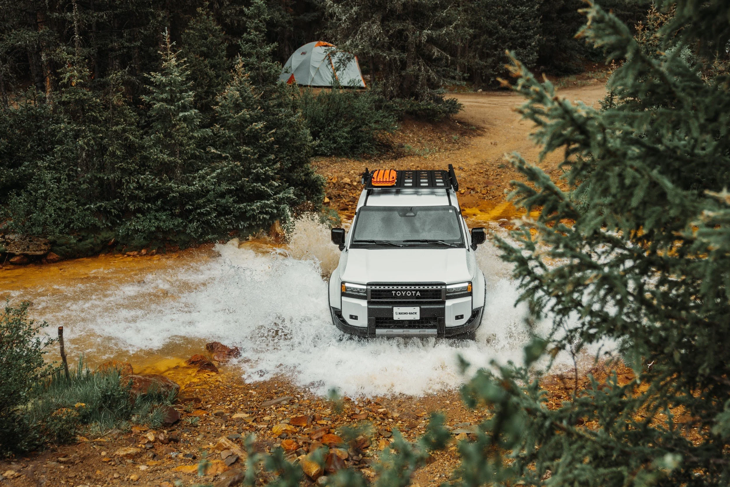 Toyota Land Cruiser with a Rhino-Rack platform splashing through an orange creek crossing in the Colorado forest.