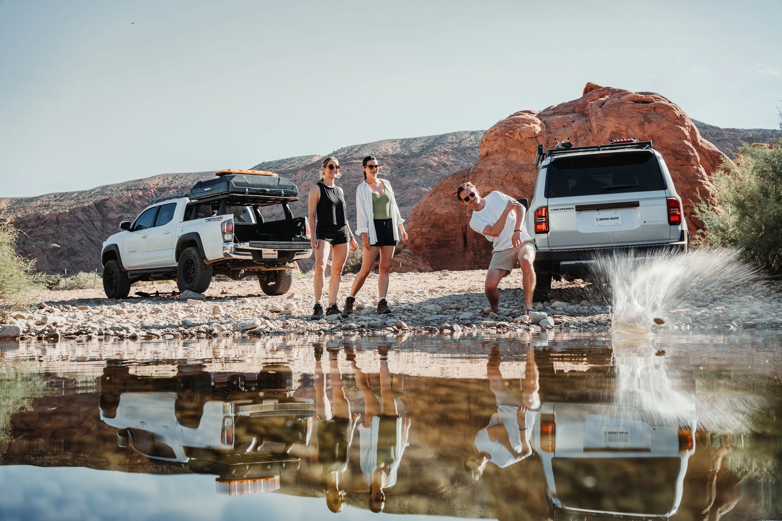 Tacoma and Land Cruiser stopped at a river in Utah, three people on the bank and a splash in the water.