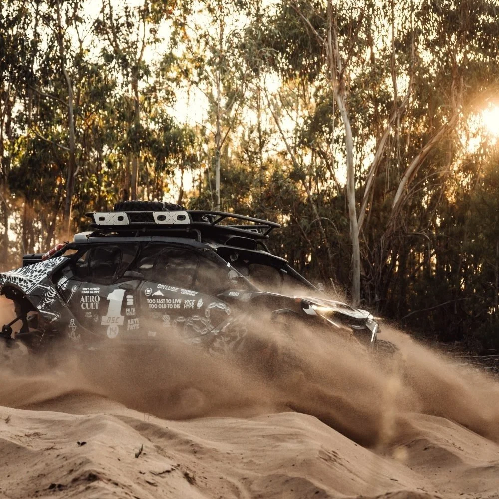 A black-and-white patterned 34° side-by-side kicking up sand in a eucalyptus forest, livery by Death Spray